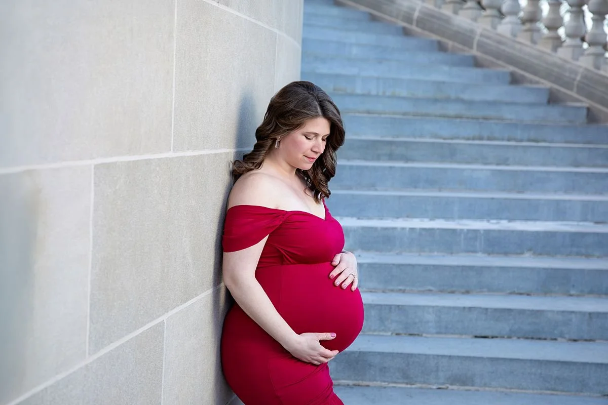 Close up maternity portrait of woman in off the shoulder red dress holding her baby bump, Sarah Kane Photography