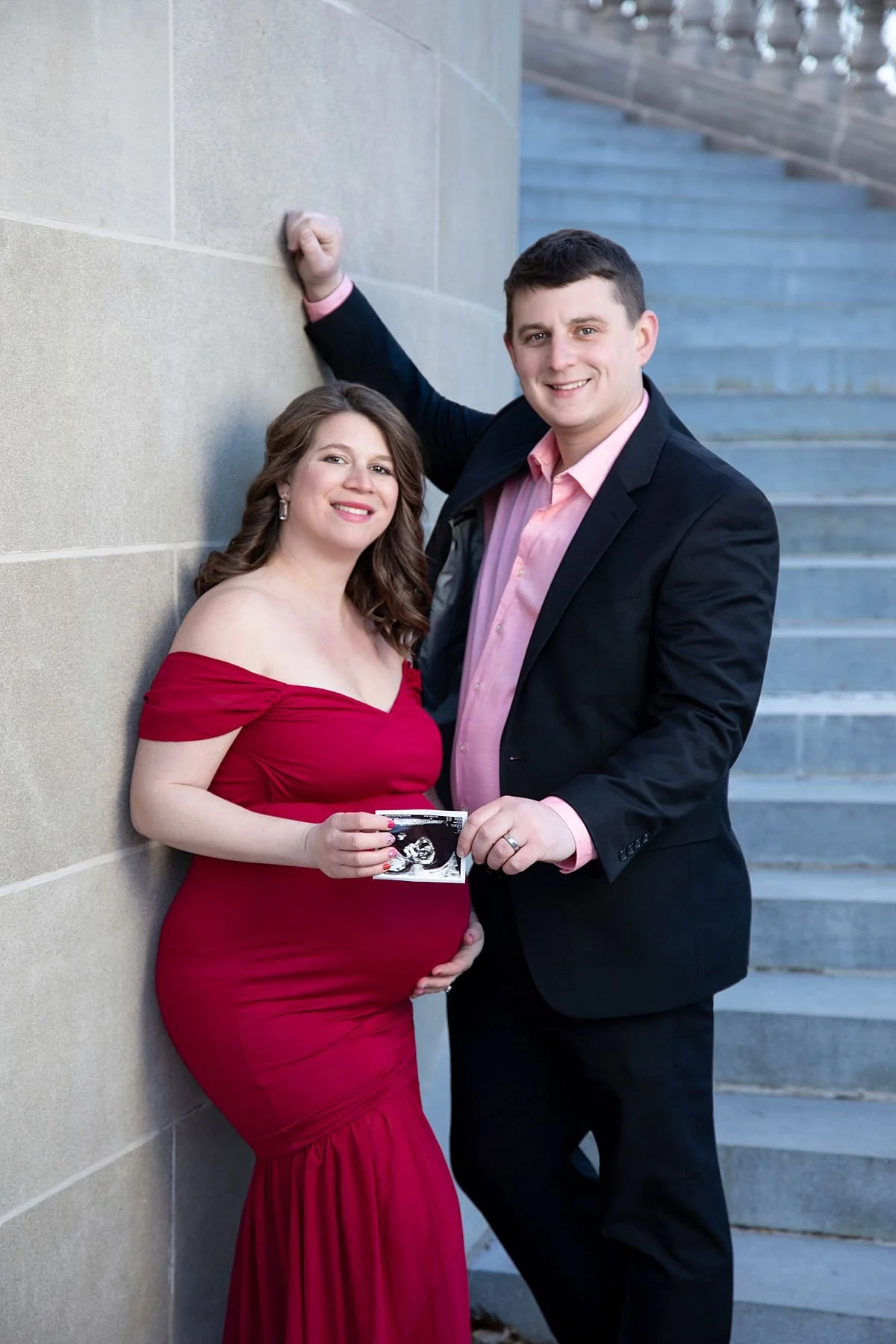 Happy expecting couple leaning against a stone wall holding an ultrasound photo, Sarah Kane Photography