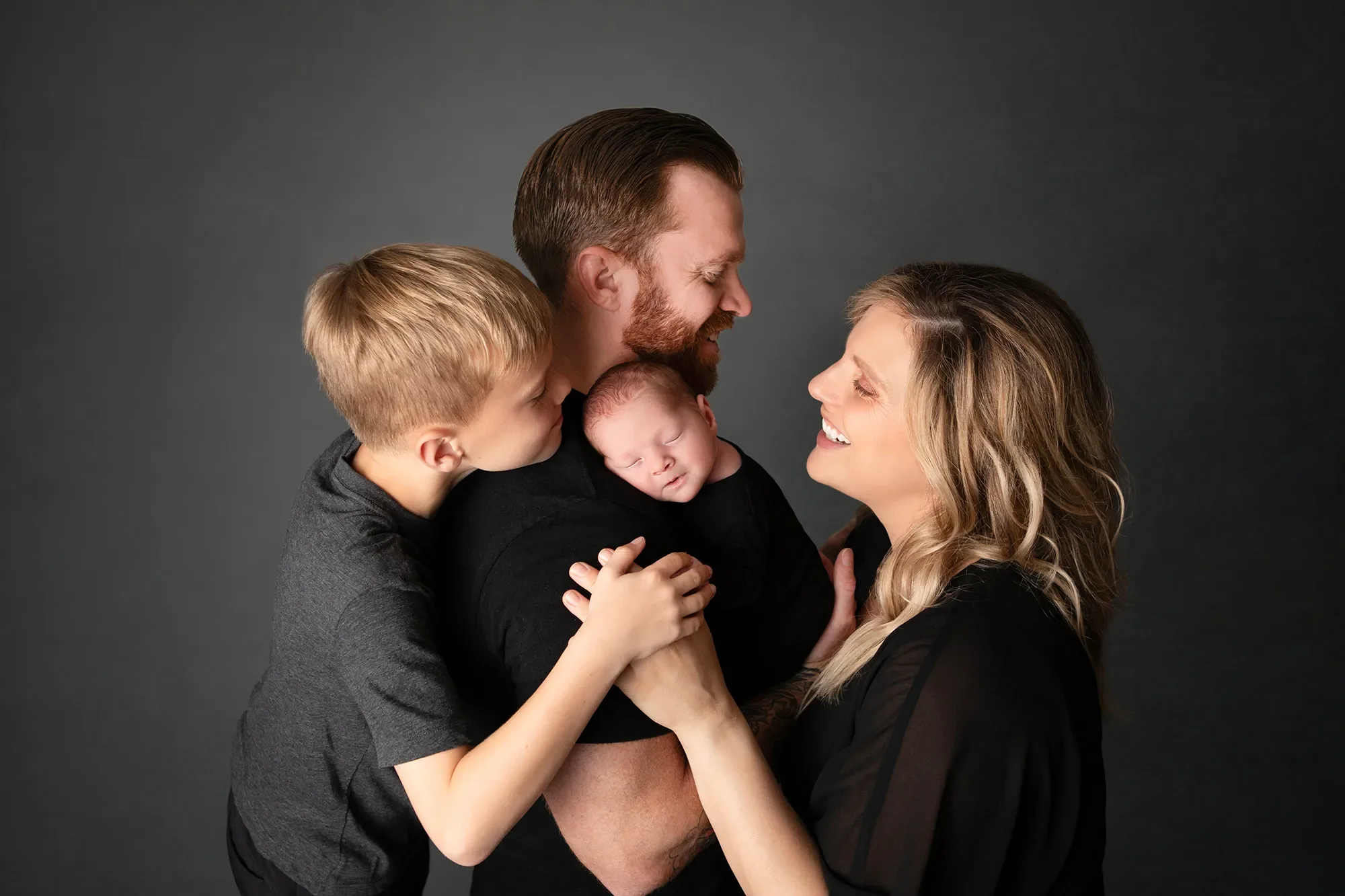 Mom, Dad, 4 year old boy and newborn baby boy posing in black and grey clothing for newborn portraits in Chesterfield Virginia with a dark grey backdrop