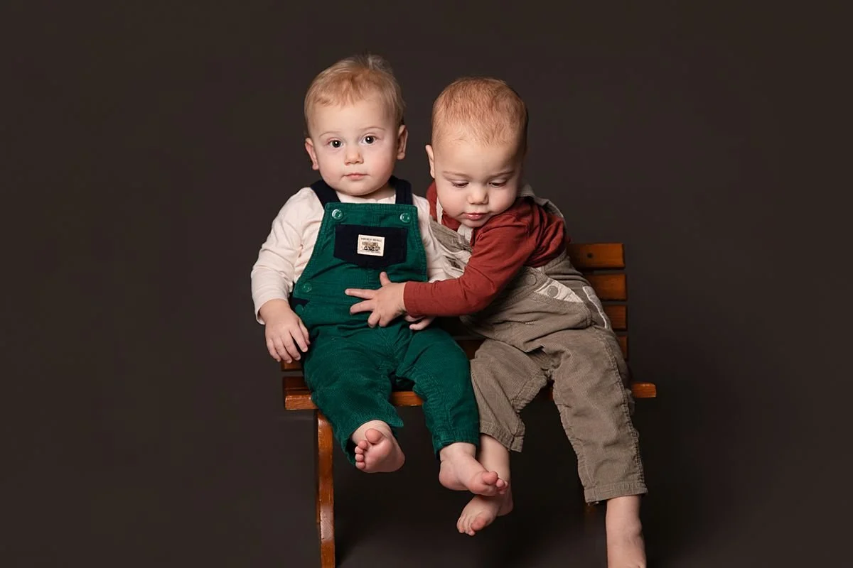 Twin one year olds on a bench while one tries to climb down by Sarah Kane Photography