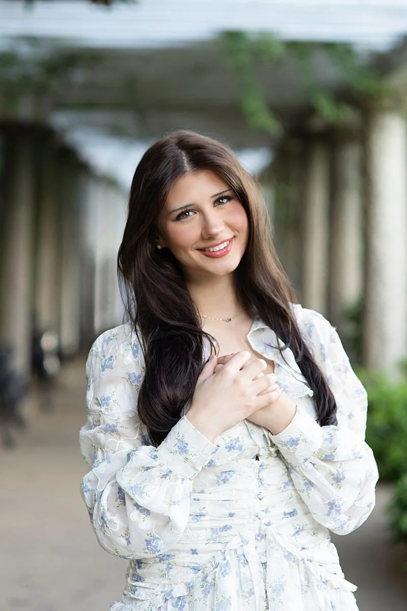 Senior girl in a blue and white floral dress with hands clasped under a garden pergola, senior portrait by Sarah Kane Photography at Maymont Park in Richmond Virginia