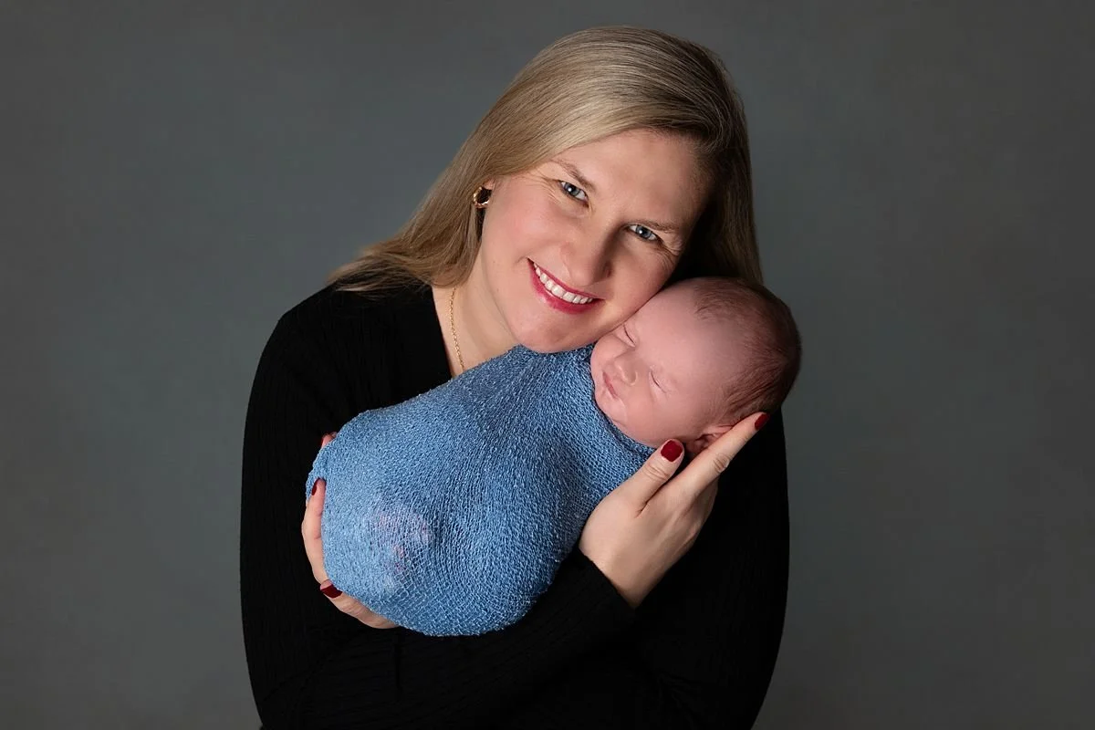 Chesterfield Virginia Newborn Photographer, Mom dressed in black holding her newborn baby wrapped in blue during professional photoshoot in Chesterfield VA close to Mechanicsville VA
