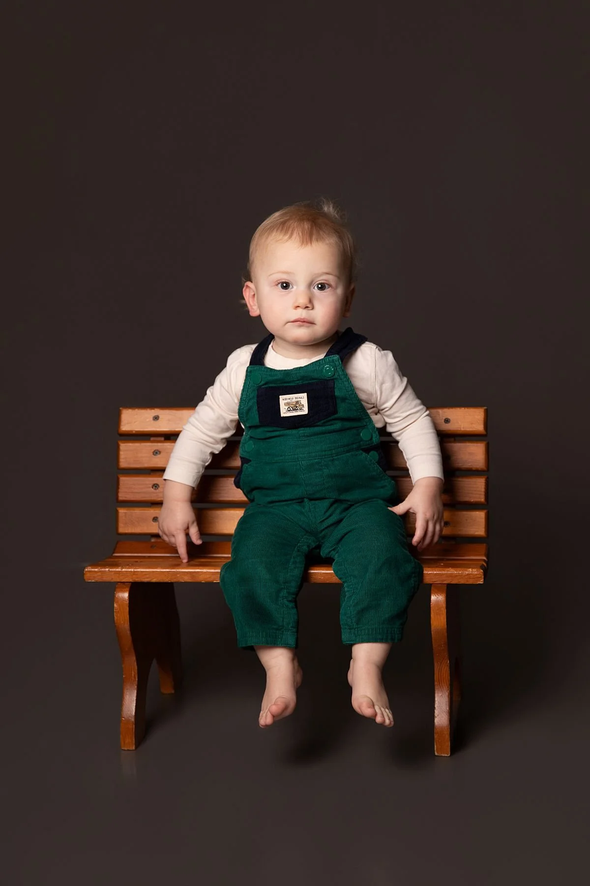 One year old twin sitting on a wooden bench facing the camera straight on by Sarah Kane Photography