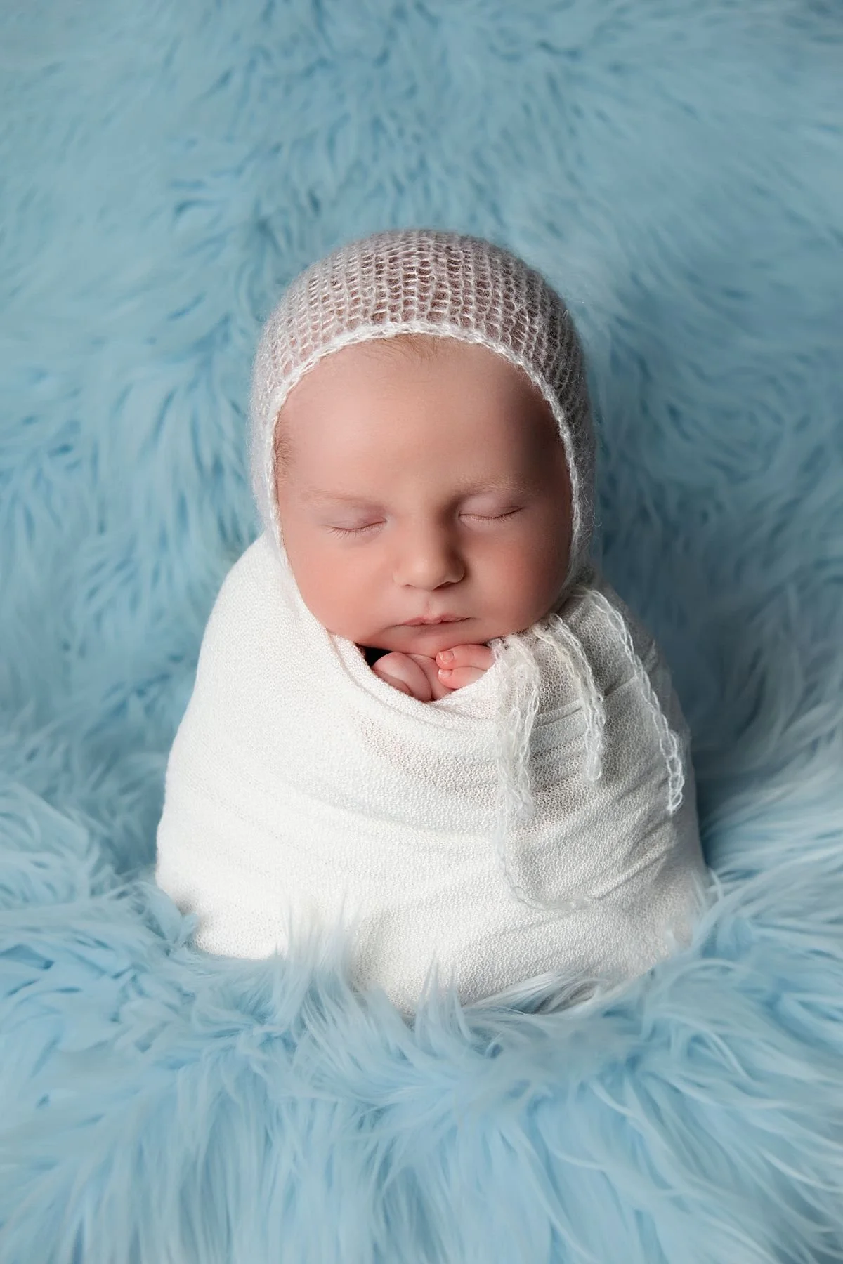 Chesterfield Virginia Newborn Photographer, Newborn baby wrapped in white with a soft white hat on a blue fluffy blanket for pictures outside of Mechanicsville VA