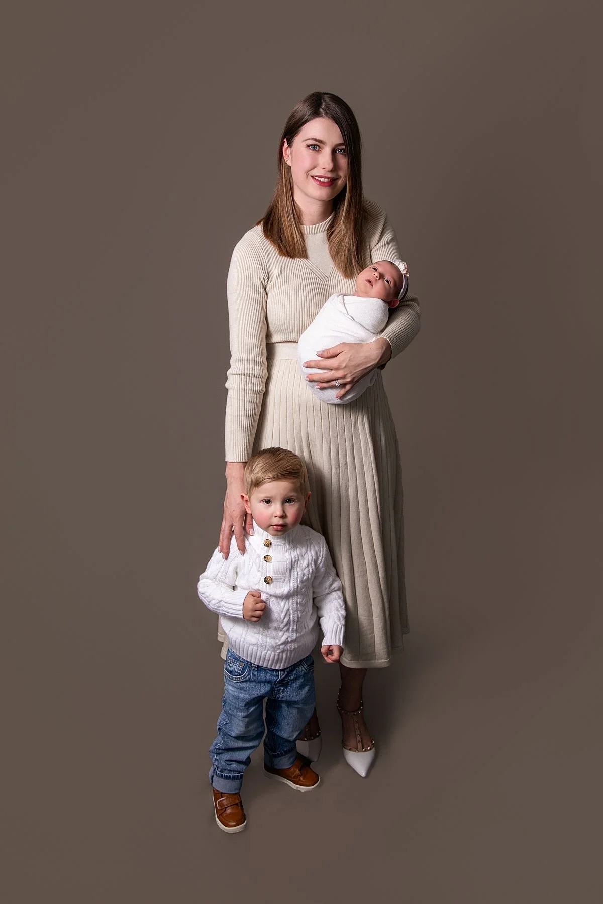 Mom holding newborn baby girl with toddler son standing in front, studio portrait, Sarah Kane Photography