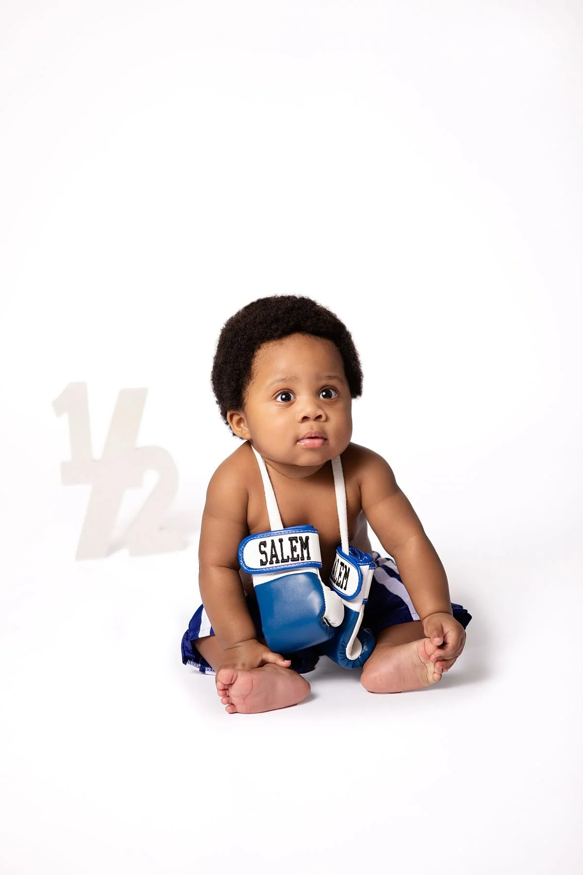 Baby Salem in boxing shorts with gloves around his neck beside a "1/2" prop by Sarah Kane Photography, Chesterfield VA