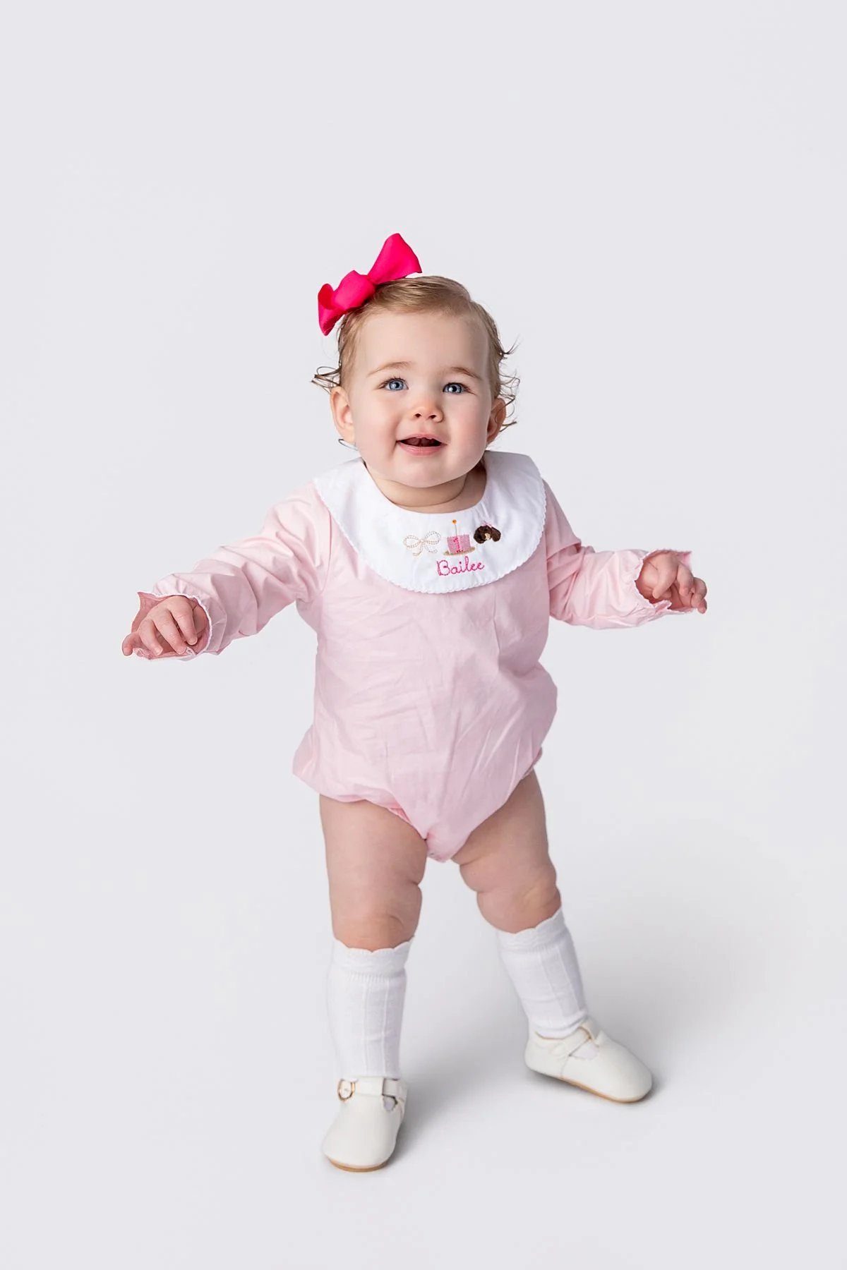 Smiling baby standing in pink romper with embroidered birthday collar, Sarah Kane Photography