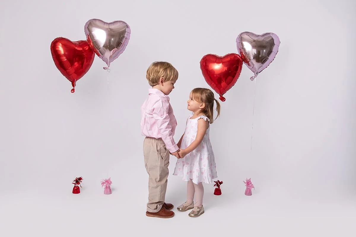 Brother and sister holding hands with valentines balloons behind them photographed by Sarah Kane Photography near Richmond VA