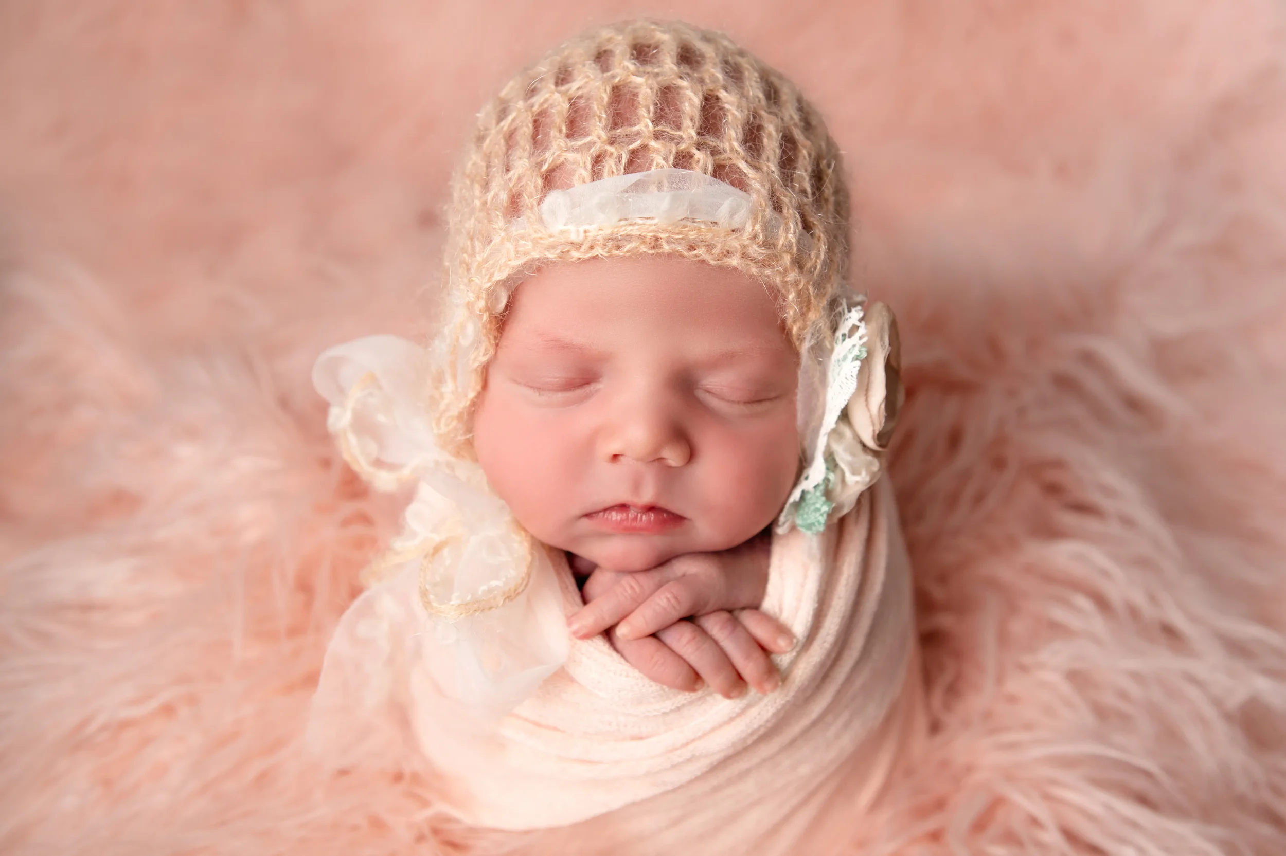 2 week old newborn baby in a peach swaddle and a knitted peach bonnet with a flower posing for newborn Portraits near Richmond Virginia