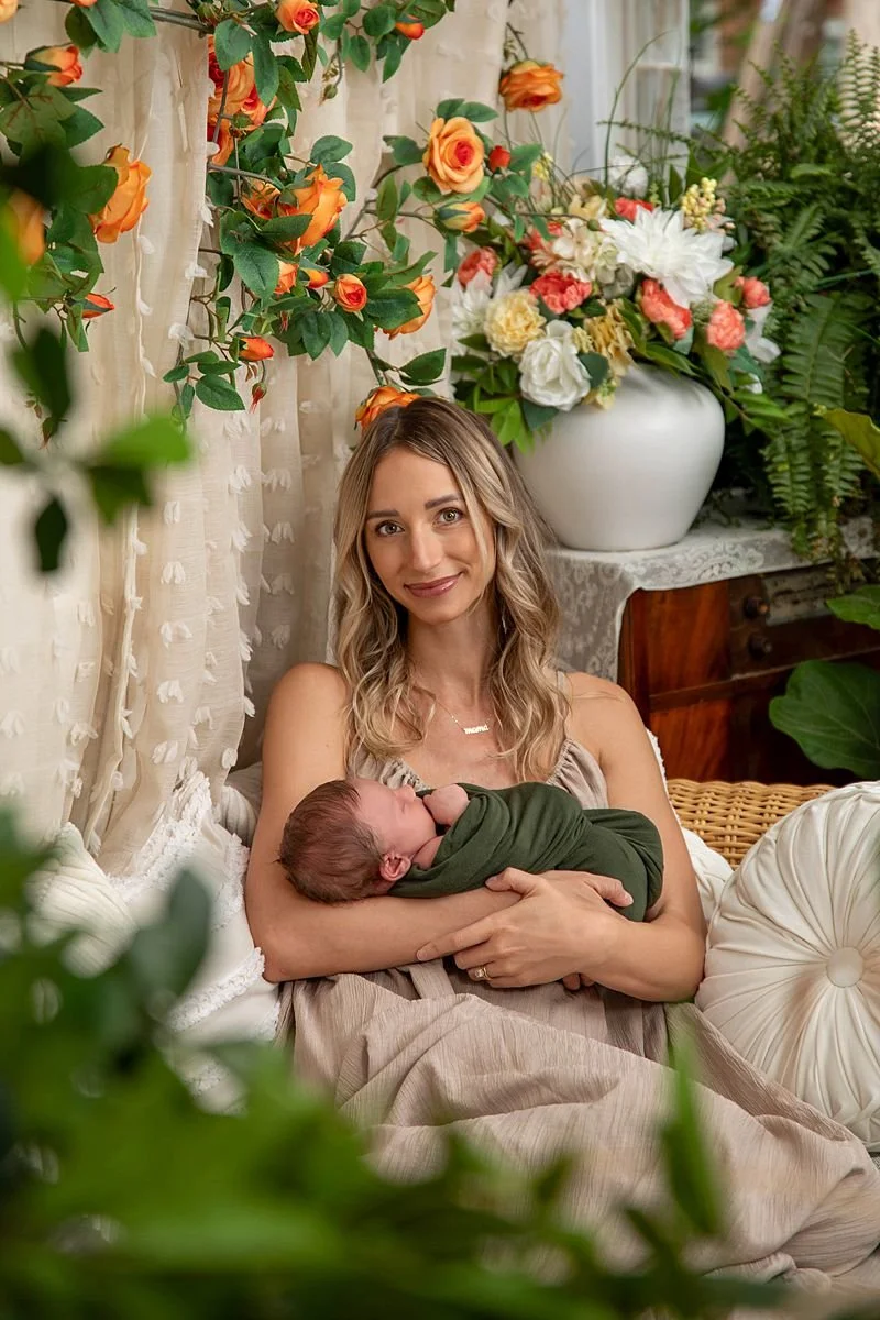 Newborn portraits with mother holding newborn son wrapped green surrounded by nature, flowers and green plants with natural light in Chesterfield Virginia