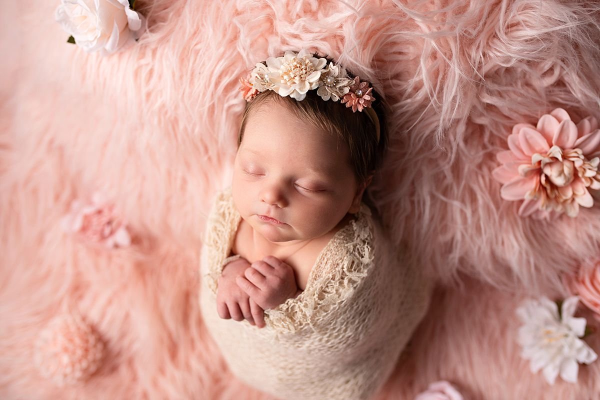 Newborn baby girl in a neutral wrap resting on a pink fur rug, Sarah Kane Photography