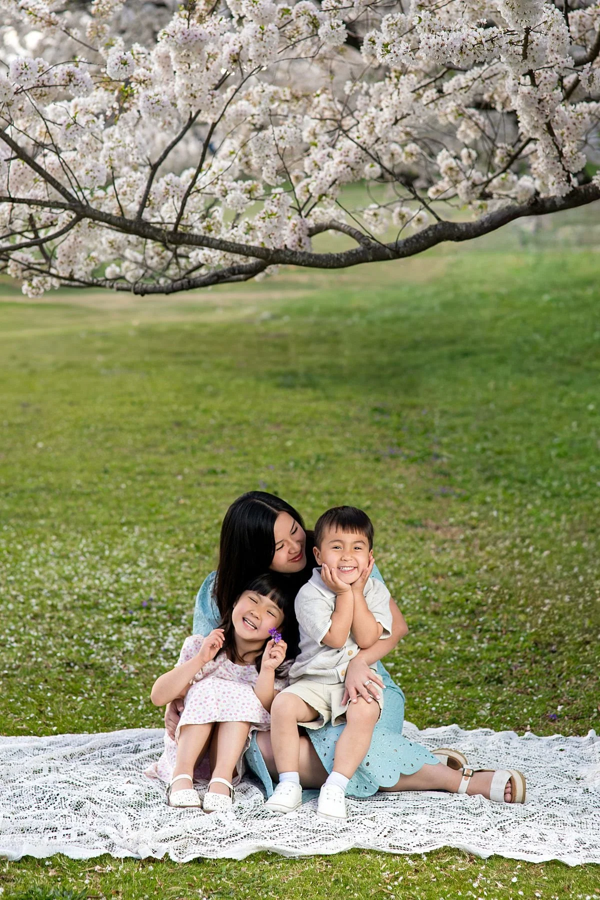 Mom sitting with her son and daughter on a lace blanket under a cherry blossom tree during a spring mini session, Sarah Kane Photography, Richmond Virginia