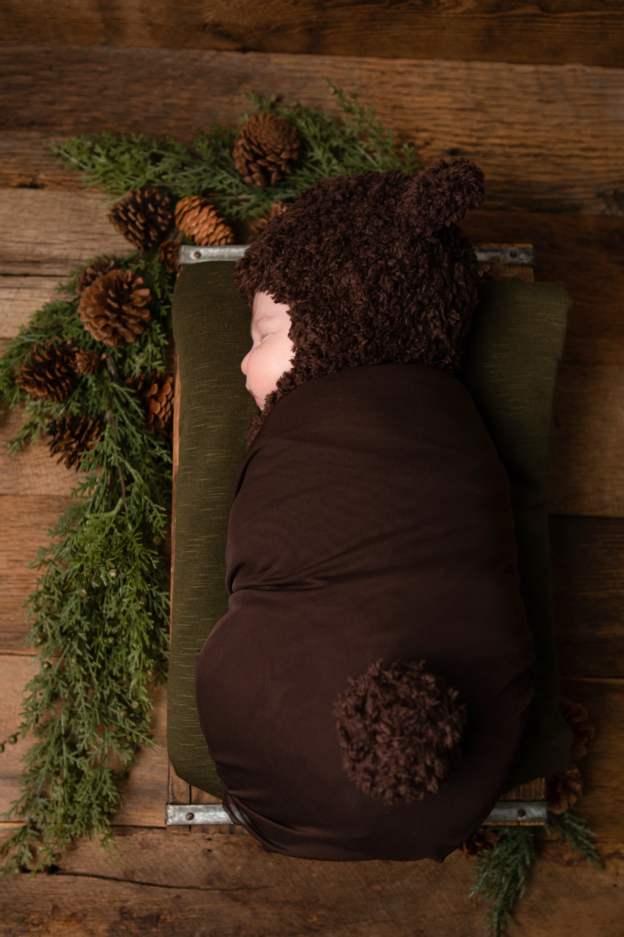 Newborn Session in My Chesterfield Virginia Studio, a newborn sleeps curled on his side in a brown bear outfit against a wooden backdrop