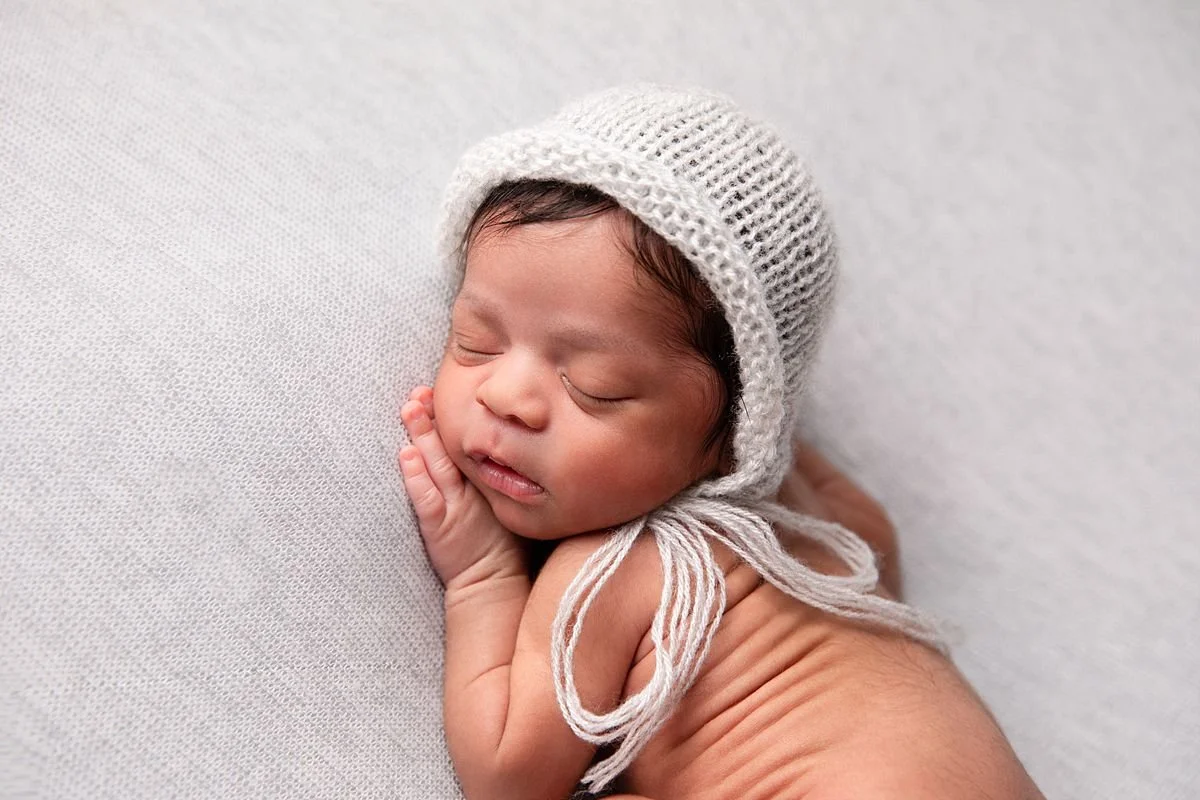 Newborn twin baby girl sleeping on her side wearing a soft knit bonnet during a studio session with Sarah Kane Photography in Chesterfield Virginia near Richmond VA.
