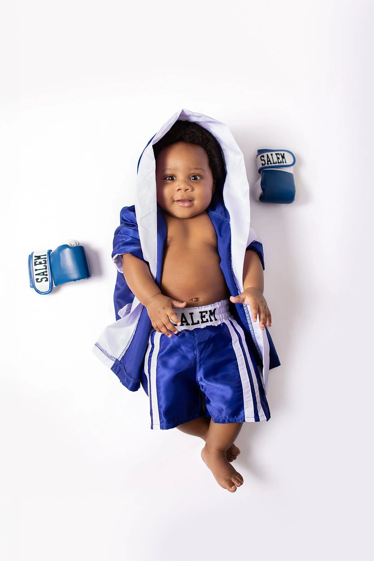 Aerial view of baby Salem smiling in a blue boxing robe and shorts with personalized gloves by Sarah Kane Photography, Chesterfield VA