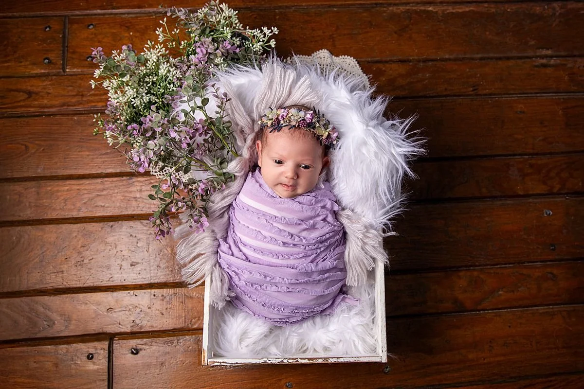 Overhead newborn portrait, baby in lavender wrap and floral crown in rustic white crate with purple flowers, Sarah Kane Photography