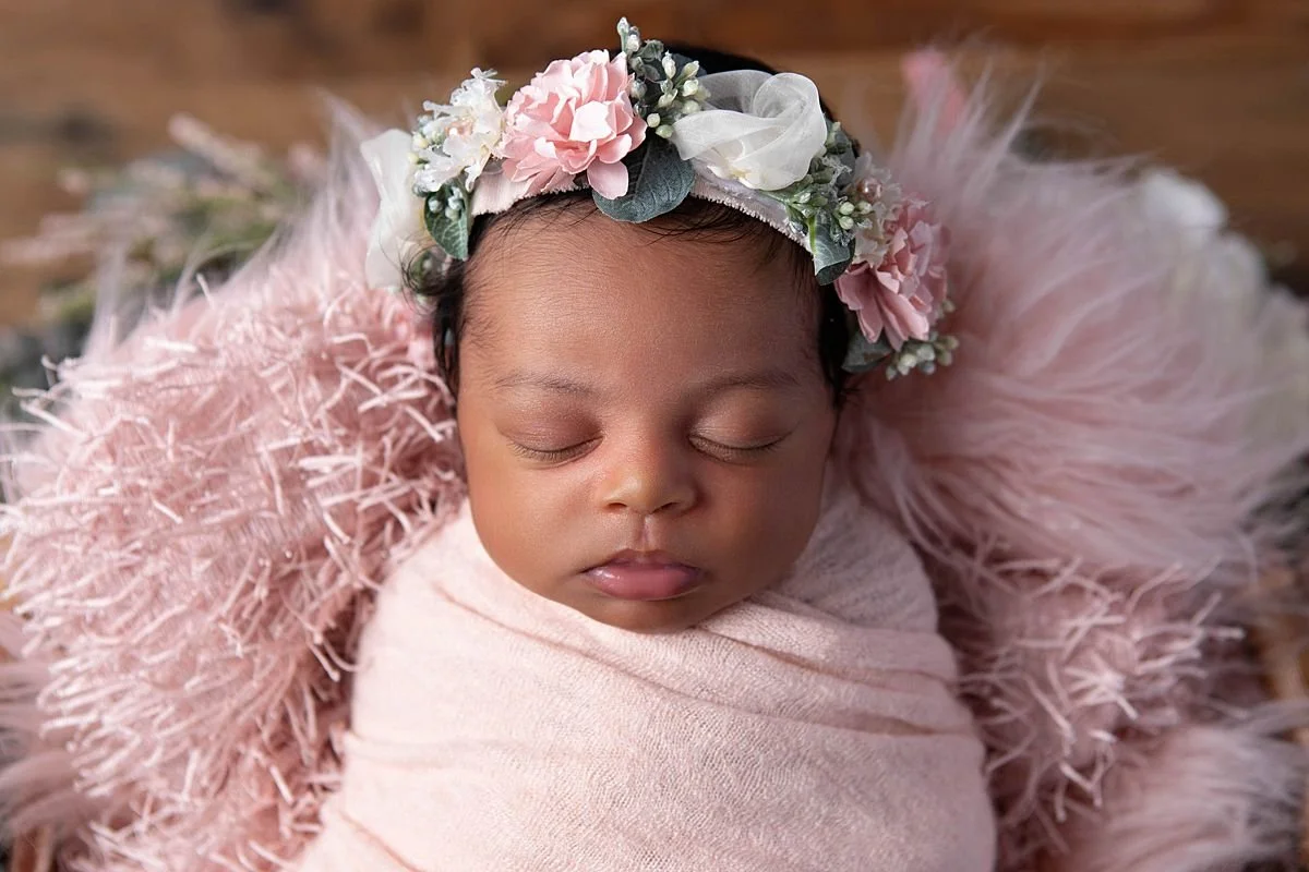 Close up of Newborn baby girl swaddled in pink wrap with floral headband during a studio newborn photo session in Chesterfield VA outside of Richmond