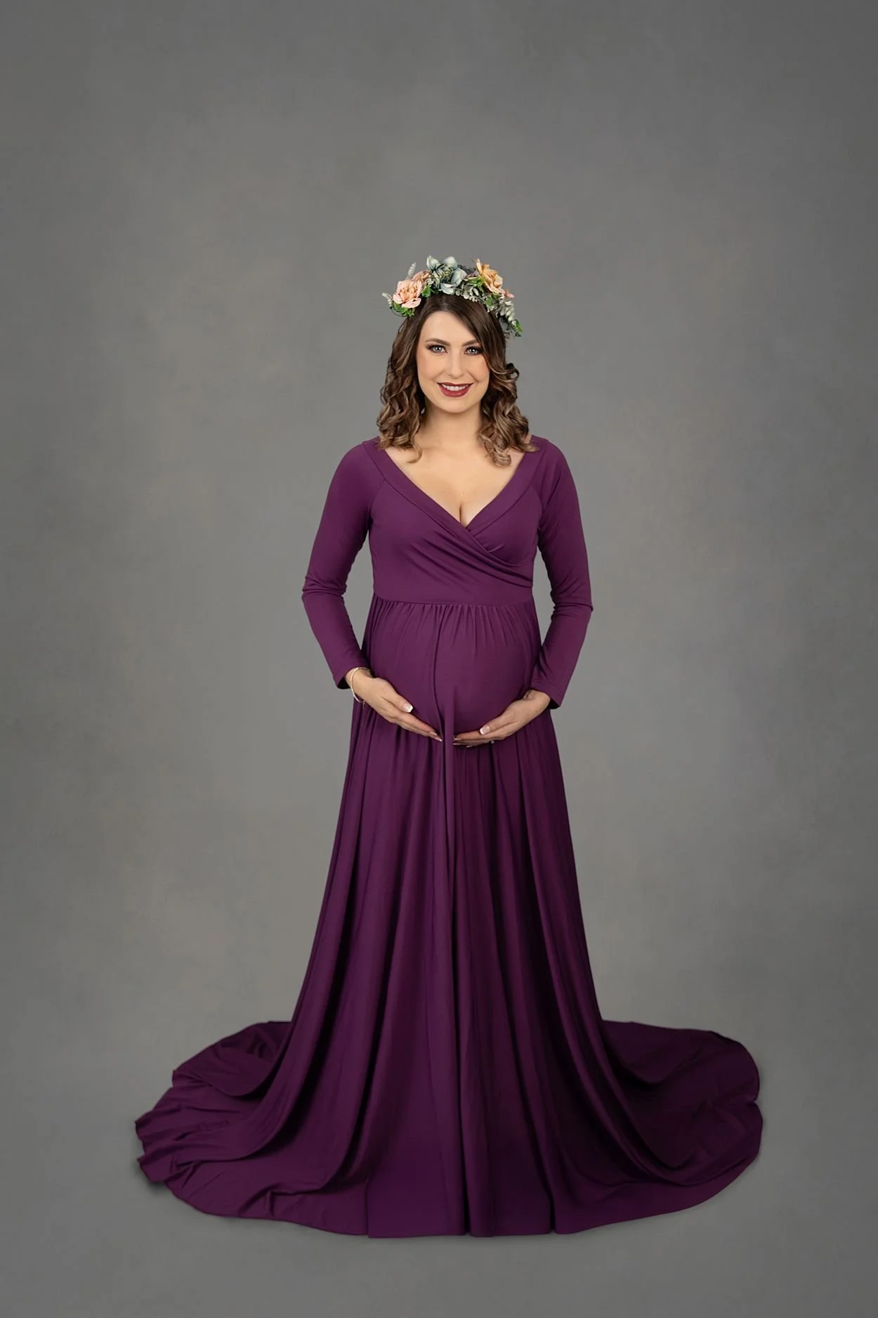 Studio Maternity Photographer in Chesterfield Virginia Just Outside of Williamsburg VA, Pregnant woman smiling and holding belly in a floor length plum dress and flower crown
