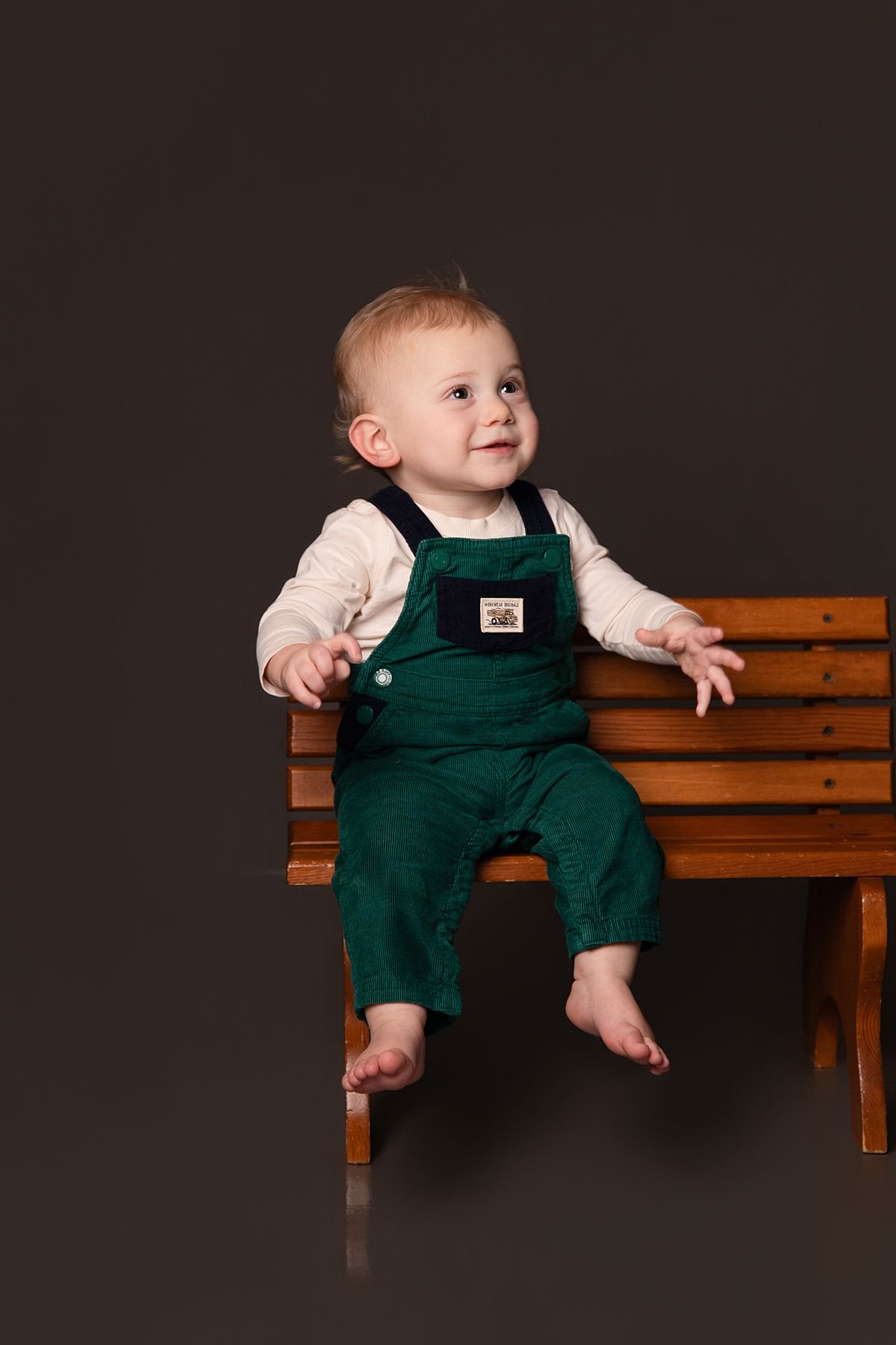 One year old twin sitting on a wooden bench smiling by Sarah Kane Photography