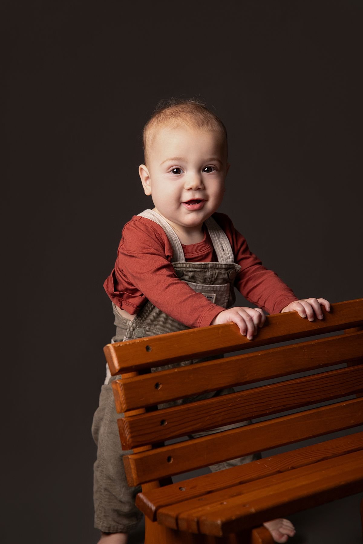One year old twin standing behind a bench with his hands on the back by Sarah Kane Photography