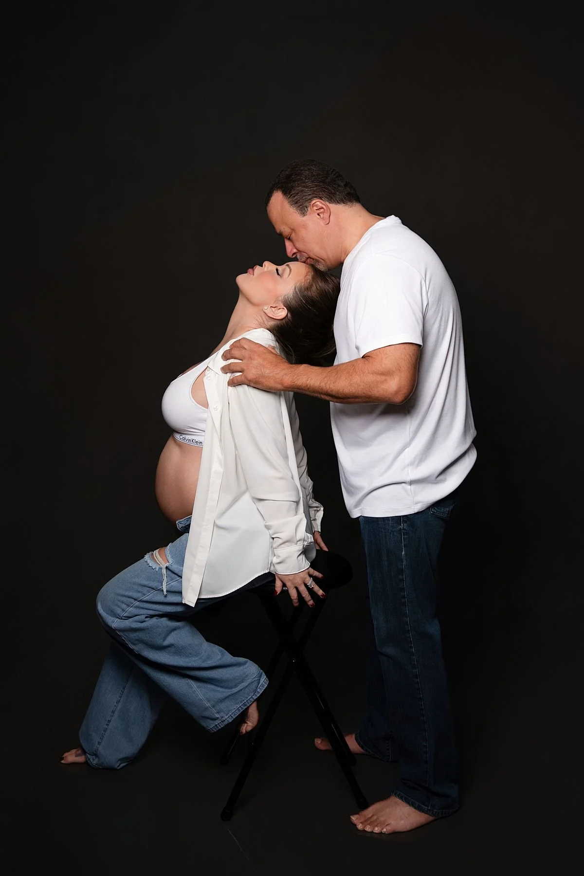 Pregnant woman leaning back against her partner who kisses her forehead, Sarah Kane Photography