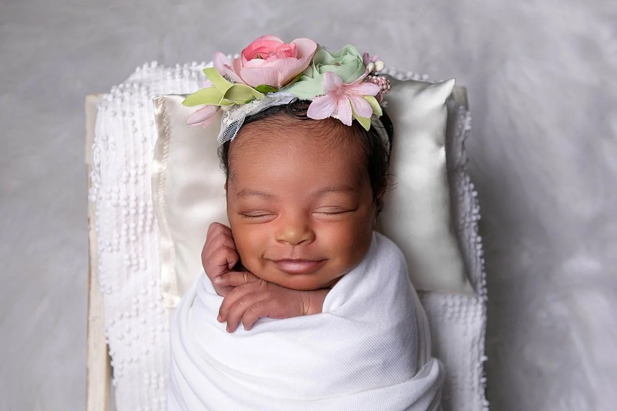 Close up newborn photo of a baby smiling wrapped in white during a studio session in Chesterfield Virginia near Richmond