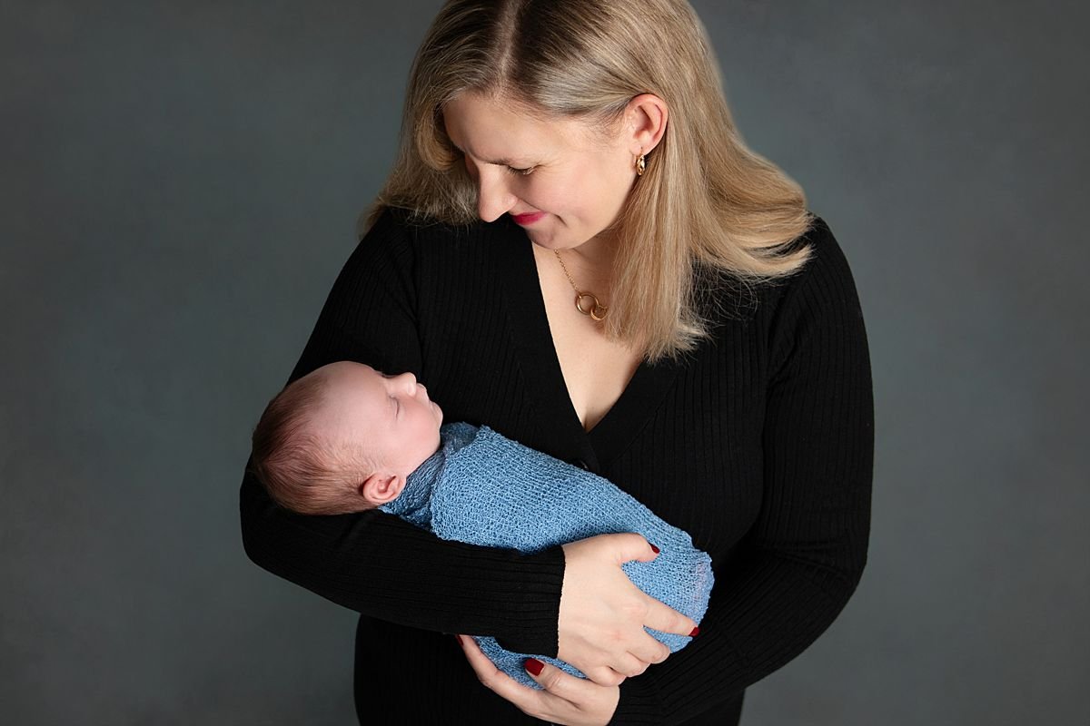 Chesterfield Virginia Newborn Photographer, Studio newborn portrait of a sleeping baby wrapped in blue in her mother's arm and mom looking down at the baby in Chesterfield Virginia