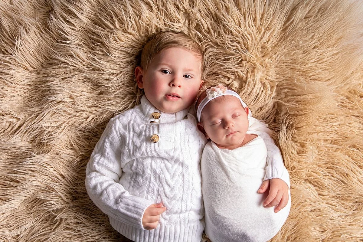 Toddler boy and sleeping newborn sister side by side on beige fur rug, Sarah Kane Photography