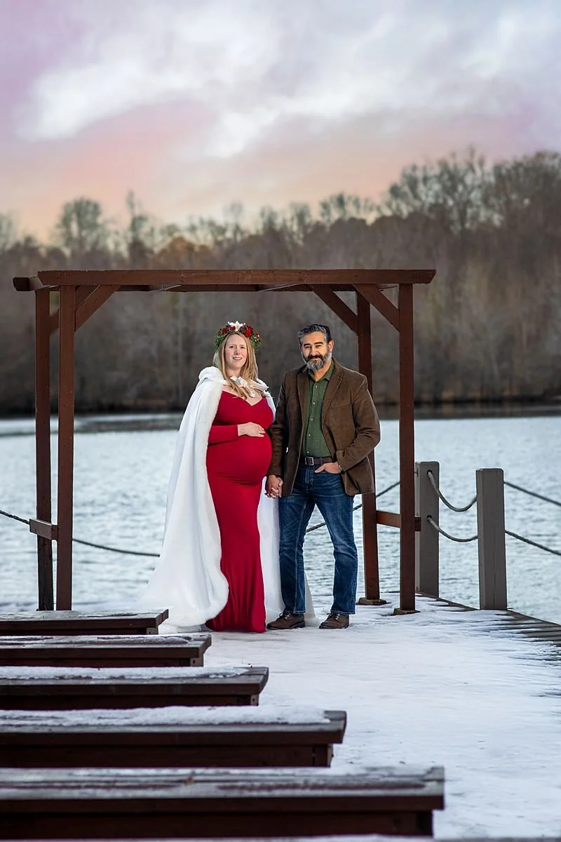 Outdoor Winter Maternity Session, Powhatan VA, Couple Hold Hands While the Pregnant Woman Touches Her Bell on a Snowy Dock by the Water