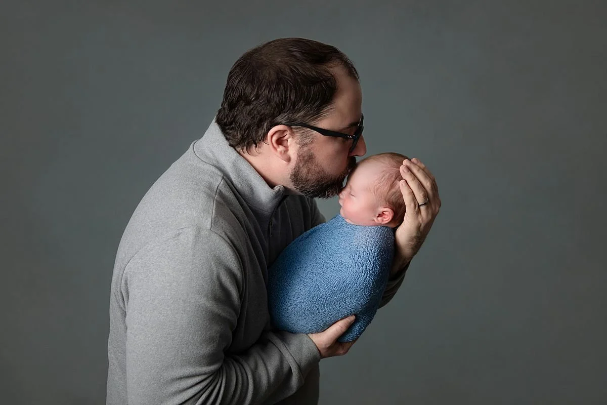 Chesterfield Virginia Newborn Photographer, Dad kissing his newborn baby wrapped in blue during a photography session close to Mechanicsville VA