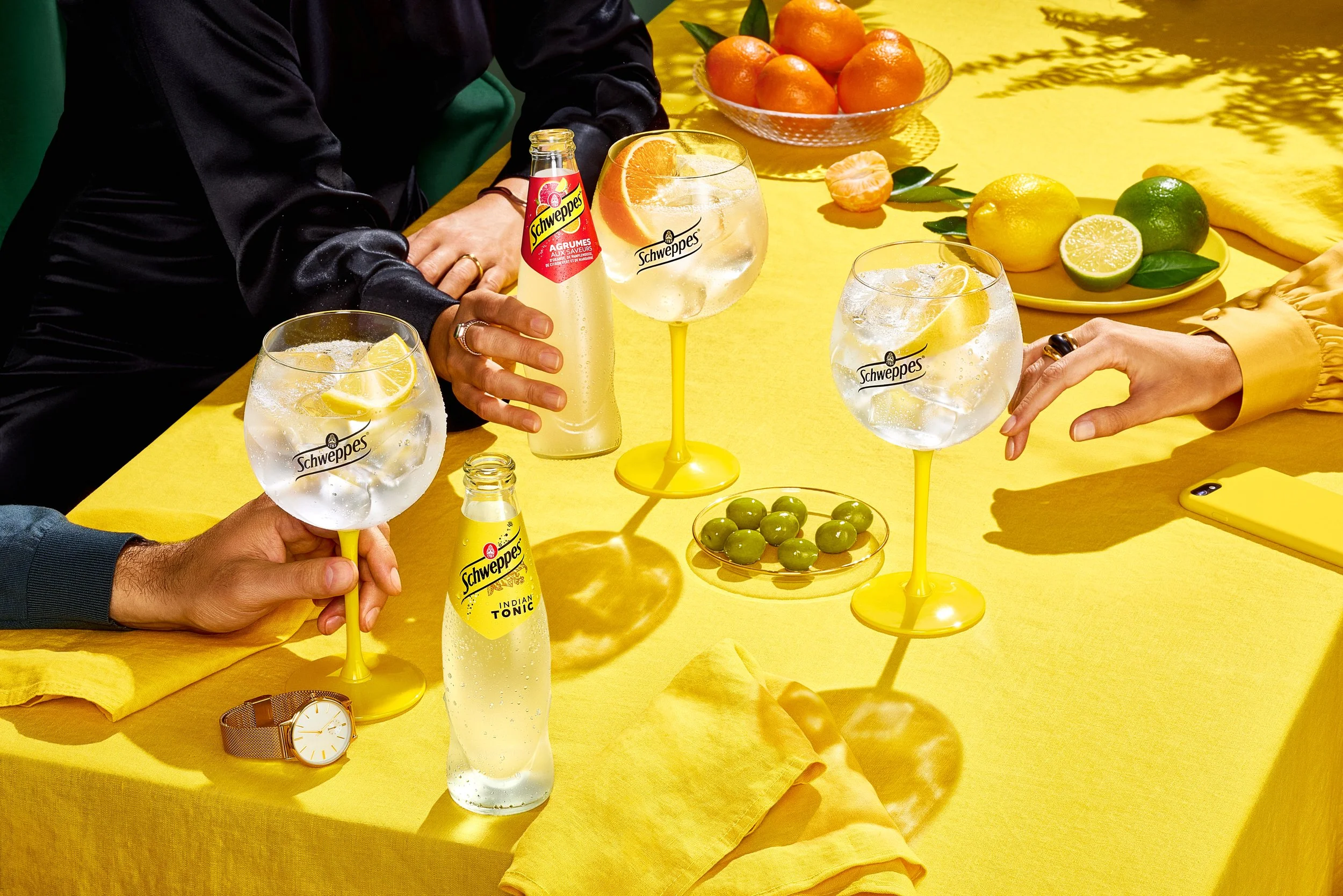 Botellas de Indian Tonic de Schweppes y Schweppes agrumes con y perfect serves en copas con hielo y cítricos sobre mesa amarilla — fotografía publicitaria para campaña Sobremesa — Alfonso + Alicia Studio