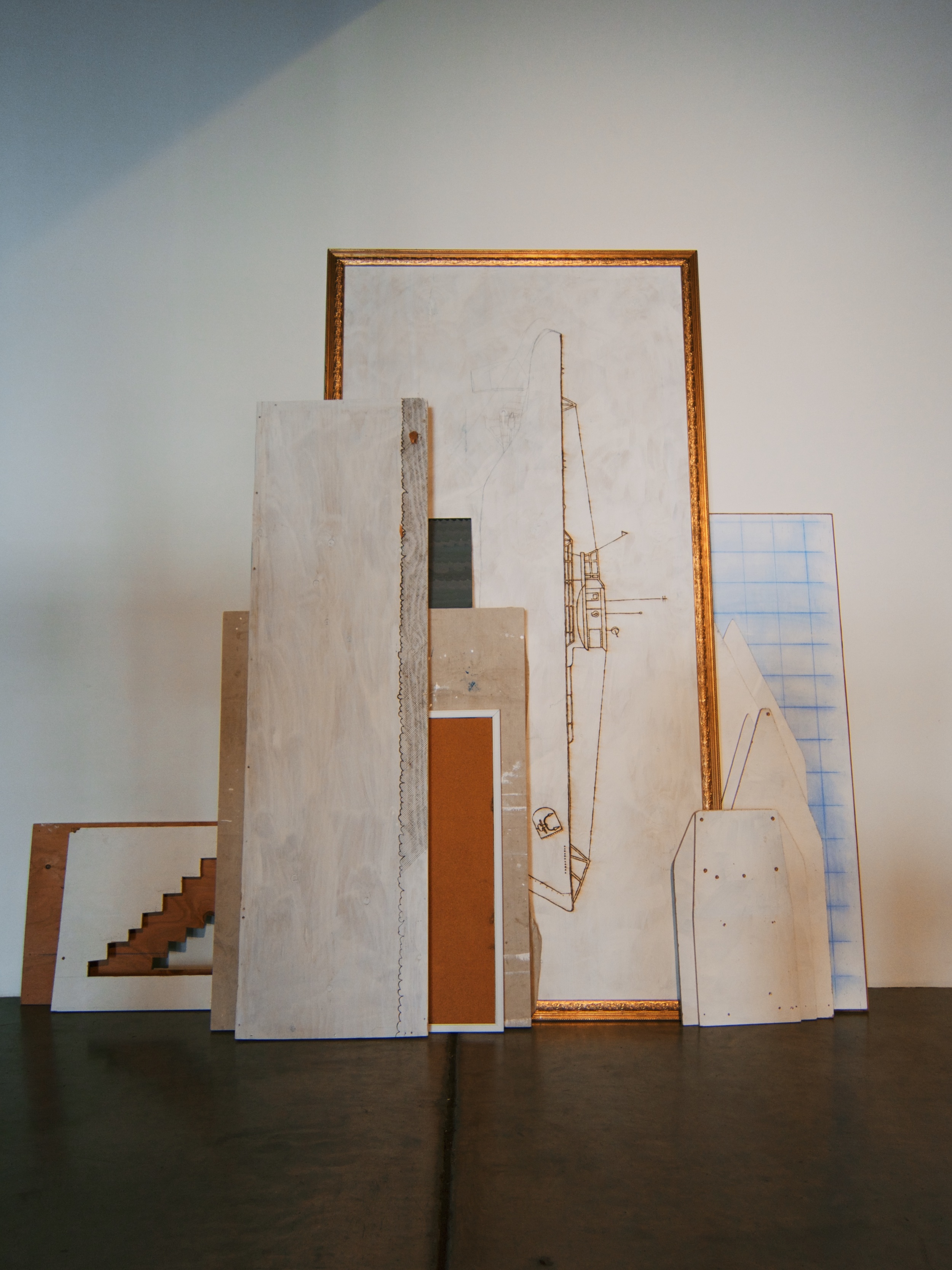  Various plywood scraps leaning against the wall containing abandoned projects that have been wood-burned, painted, and cut into, 8x8 feet, 2014. 