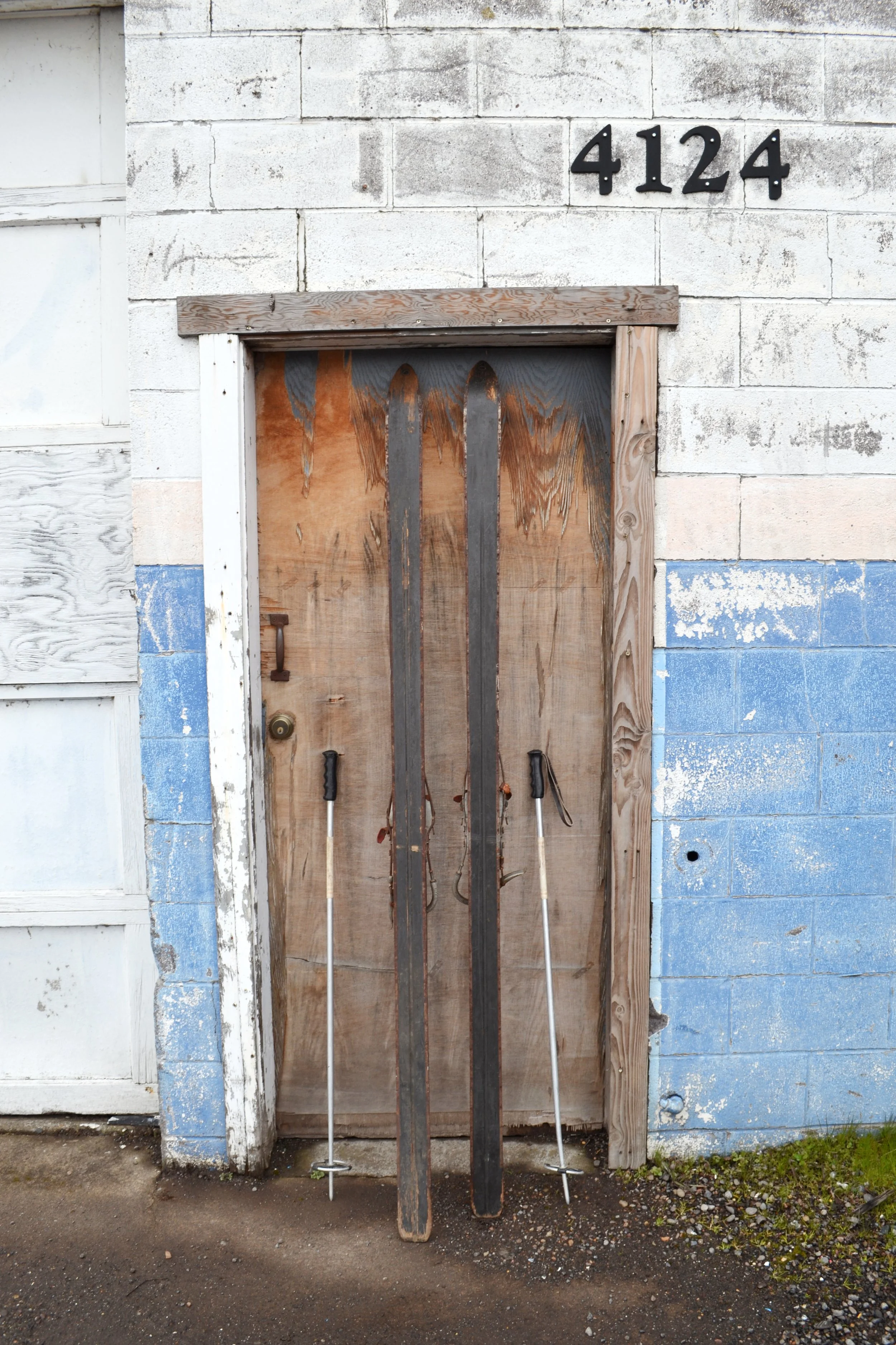 Backside of vintage wooden snow skis with a dark finish and rustic metal bindings with vintage metal ski poles.