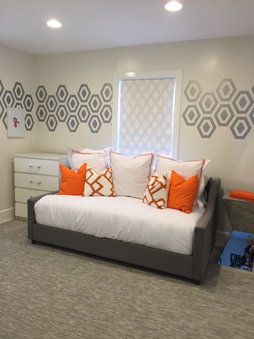 Hexagon geometric pattern vinyl wall decals in metallic silver on white wall behind a daybed, bright orange throw pillows in a guest room.