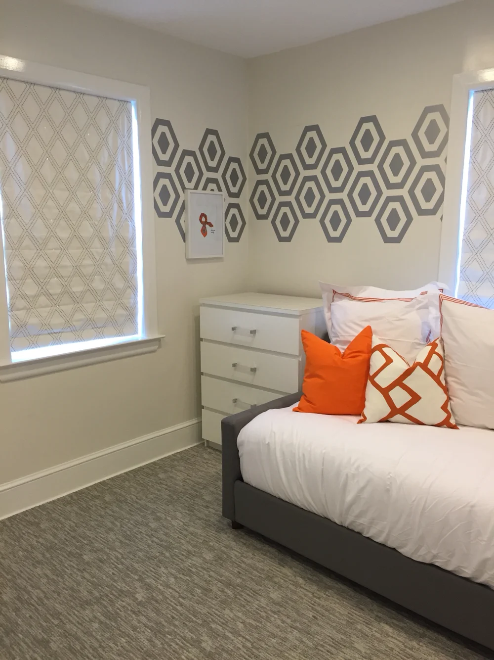 Hexagon geometric pattern vinyl wall decals in metallic silver on white wall behind a daybed, bright orange throw pillows in a guest room.
