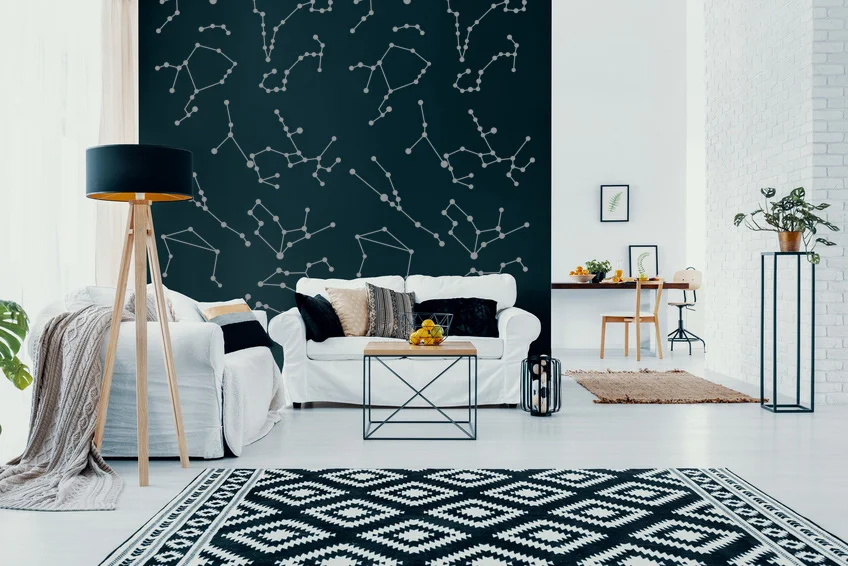 Zodiac constellation wall decals shown in metallic silver installed on a black wall of a modern living room with a white couch and a black and white geometric area rug.