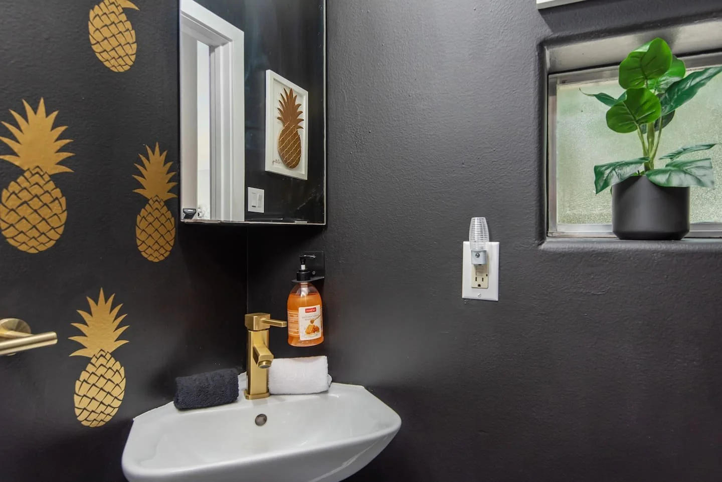 Metallic gold pineapple wall decals by Wall Star Graphics installed on a black wall in a modern bathroom.