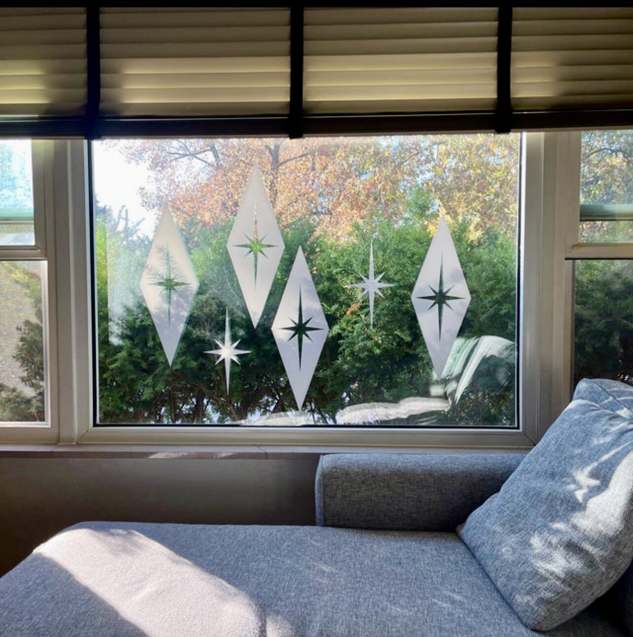 Mid century atomic style wall decals consisting of large diamond shapes with atomic stars shown in white on an interior window with a modern chaise in front.