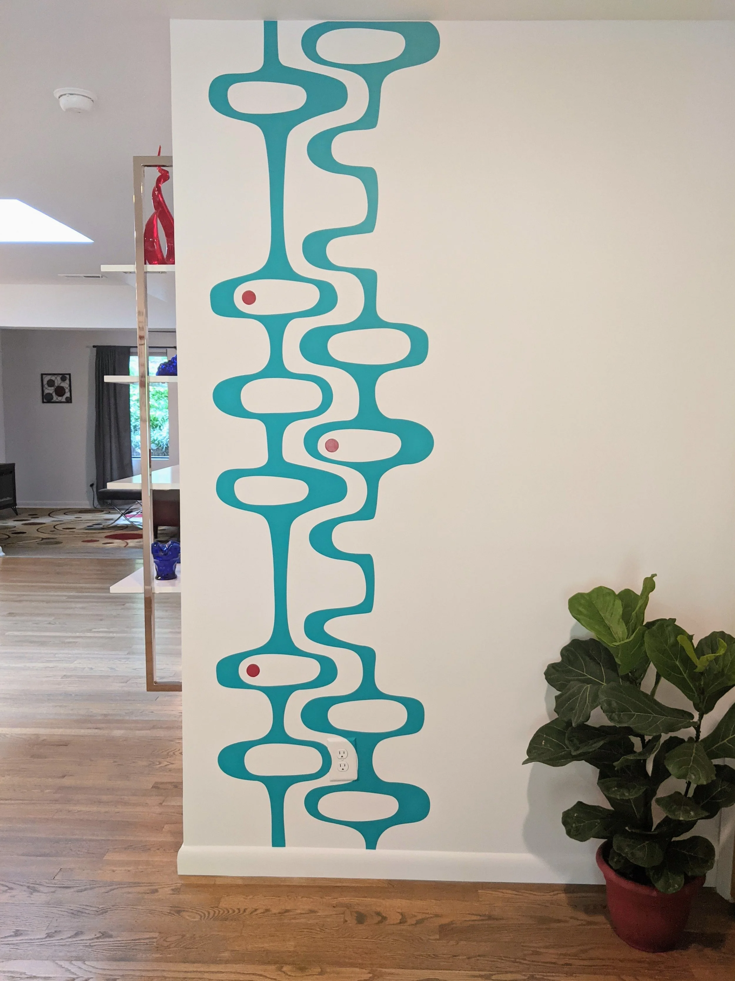 Mid Century geometric pattern wall decal by Wall Star Graphics shown in turquoise with red dots on a white wall in an entryway with a potted plant.