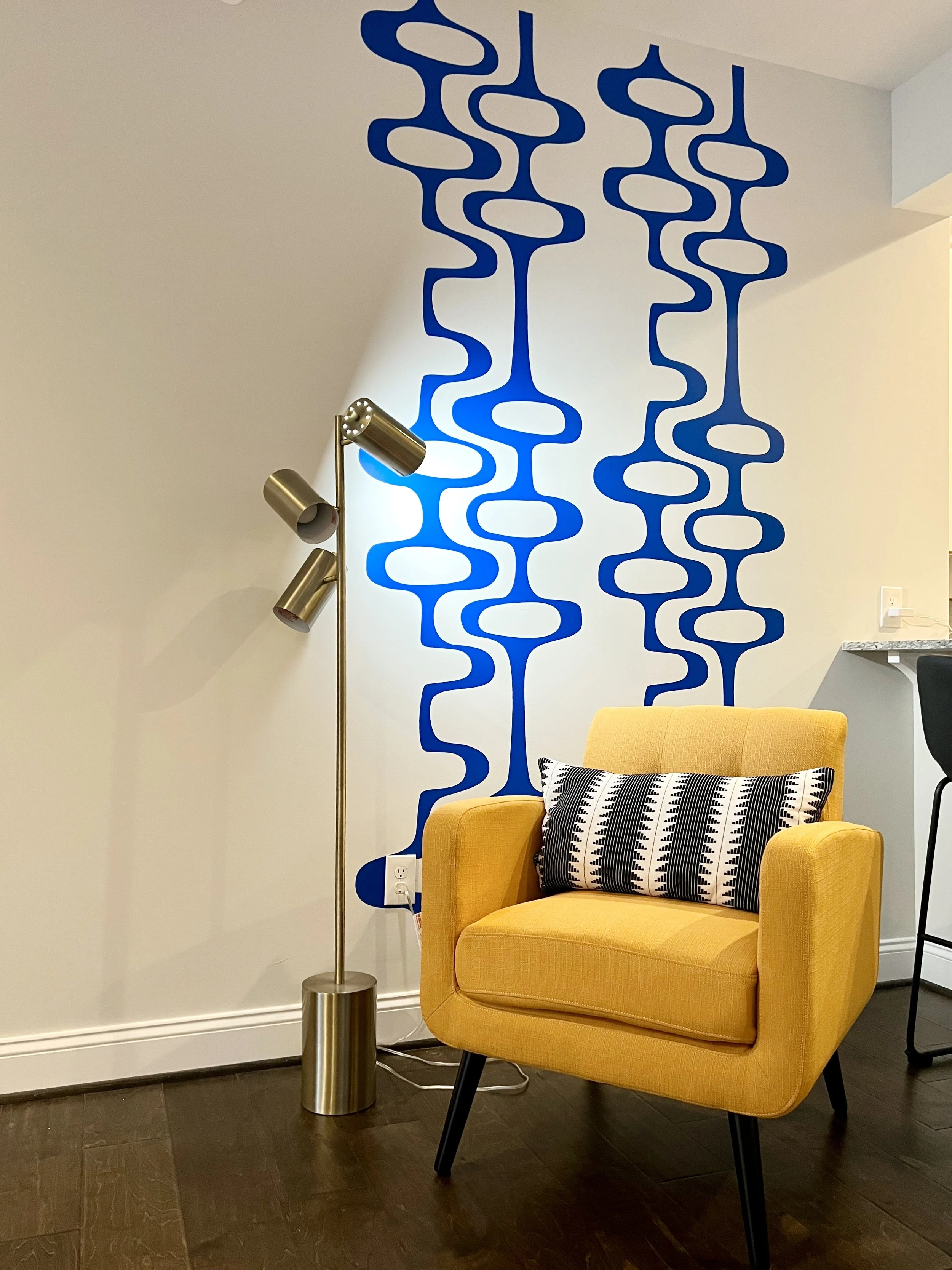 Mid Century geometric pattern wall decal by Wall Star Graphics shown in blue on a white wall behind a yellow chair with a modern floor lamp