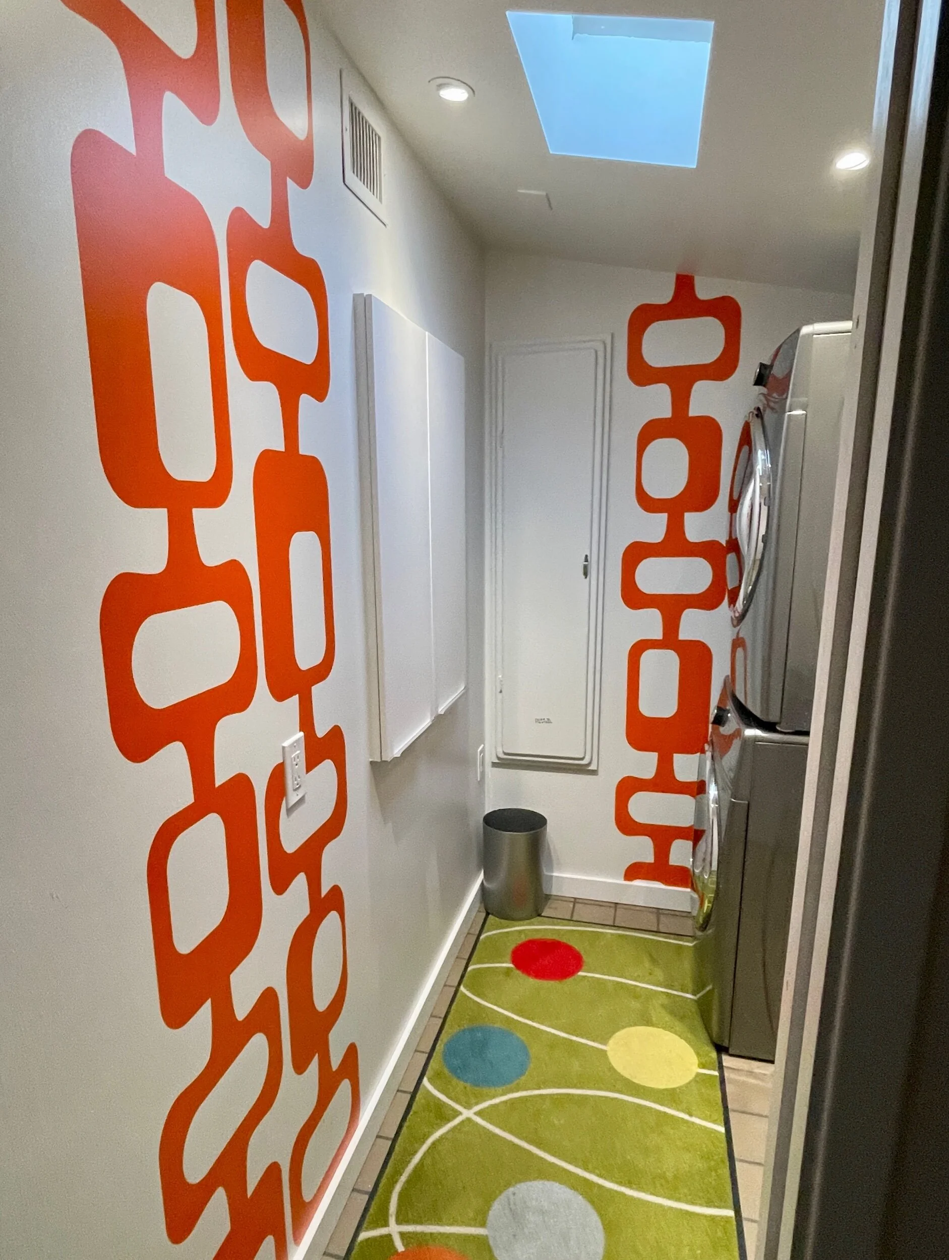 A mid century geometric pattern wall decal shown in orange on a white wall in a laundry room.