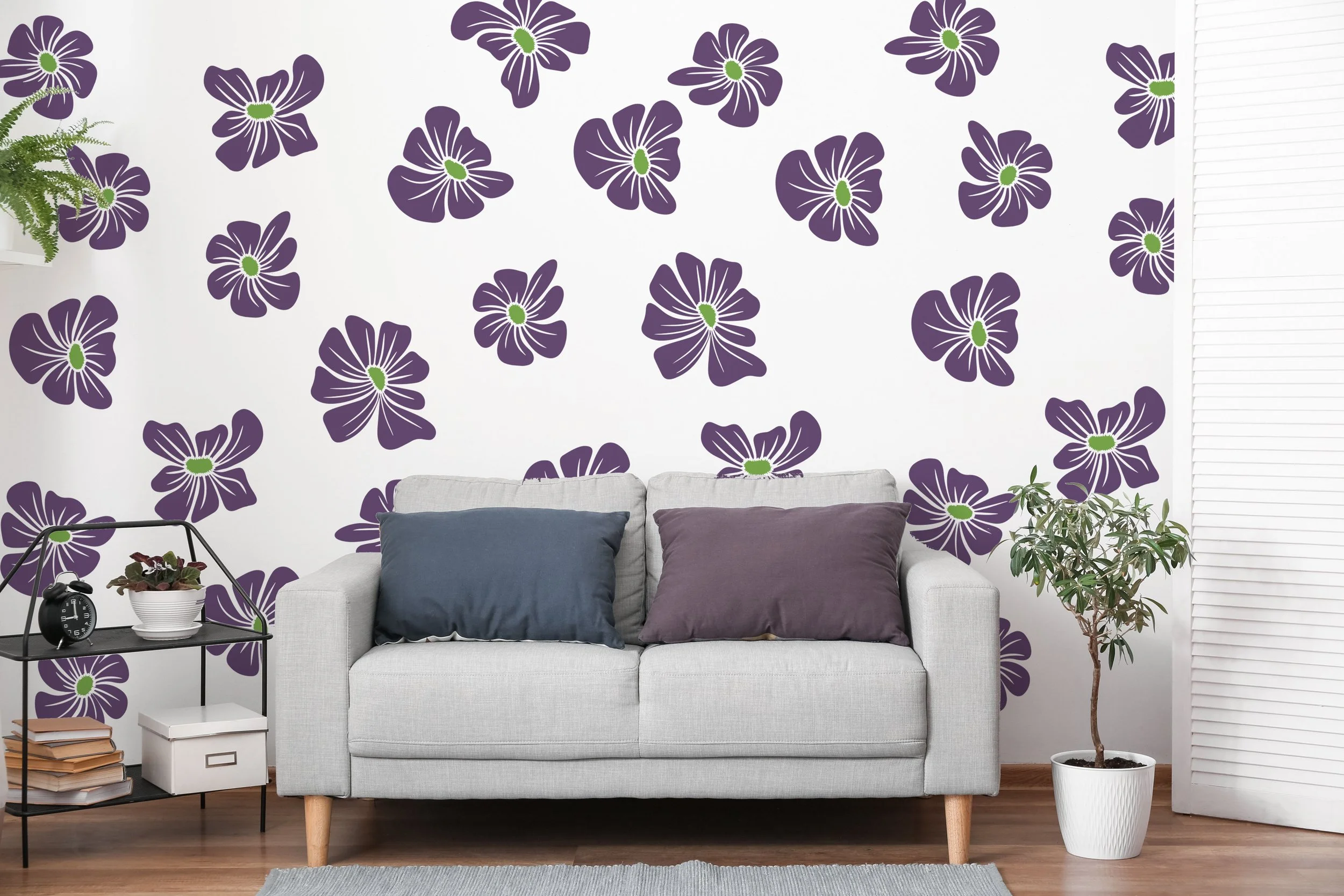 Retro groovy, two color flower wall decals shown in purple and lime green on a white wall above a modern light grey couch with blue and purple throw pillows.