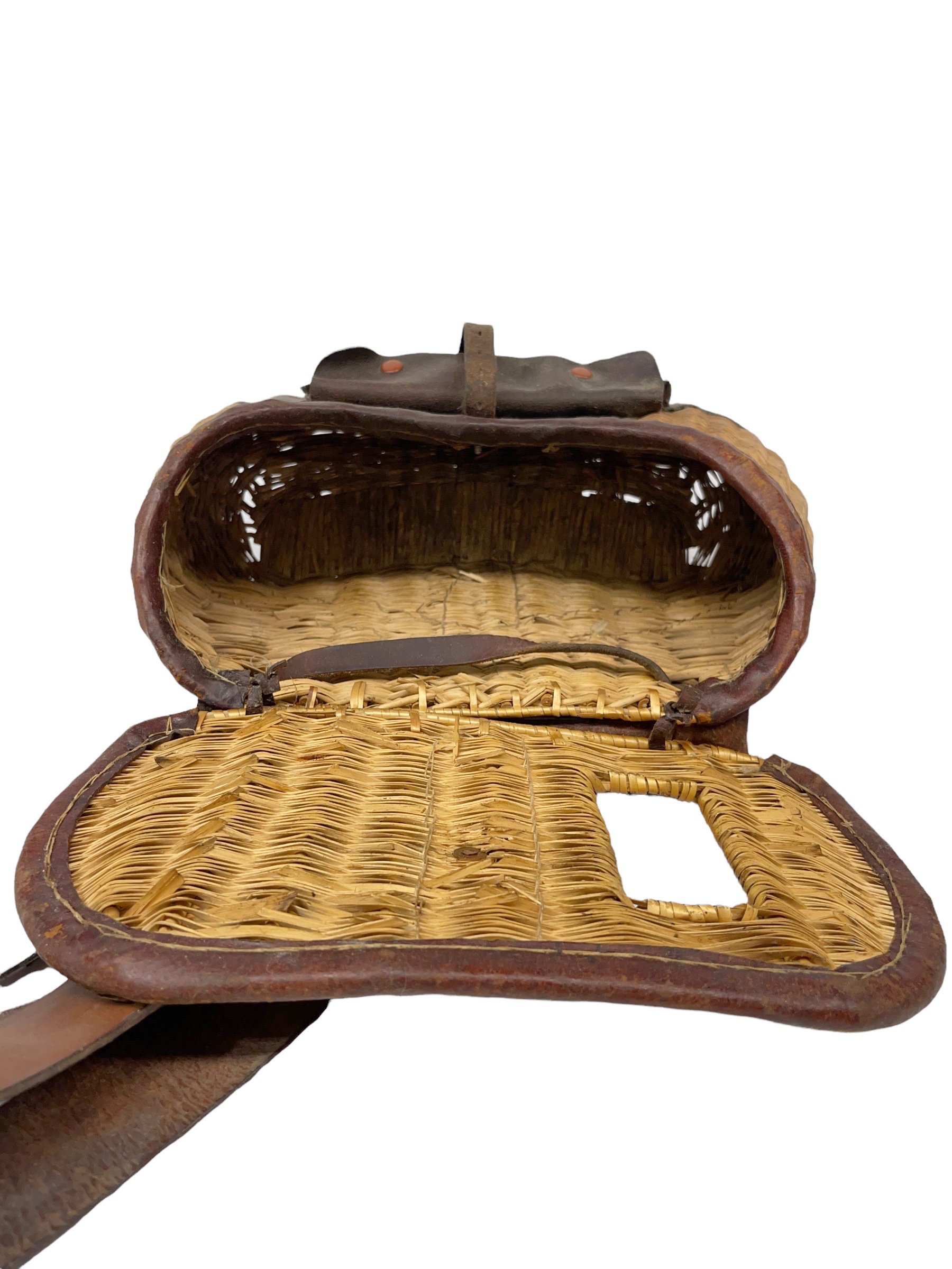 A vintage wicker fishing creel basket with strap, lid, and leather front pocket.