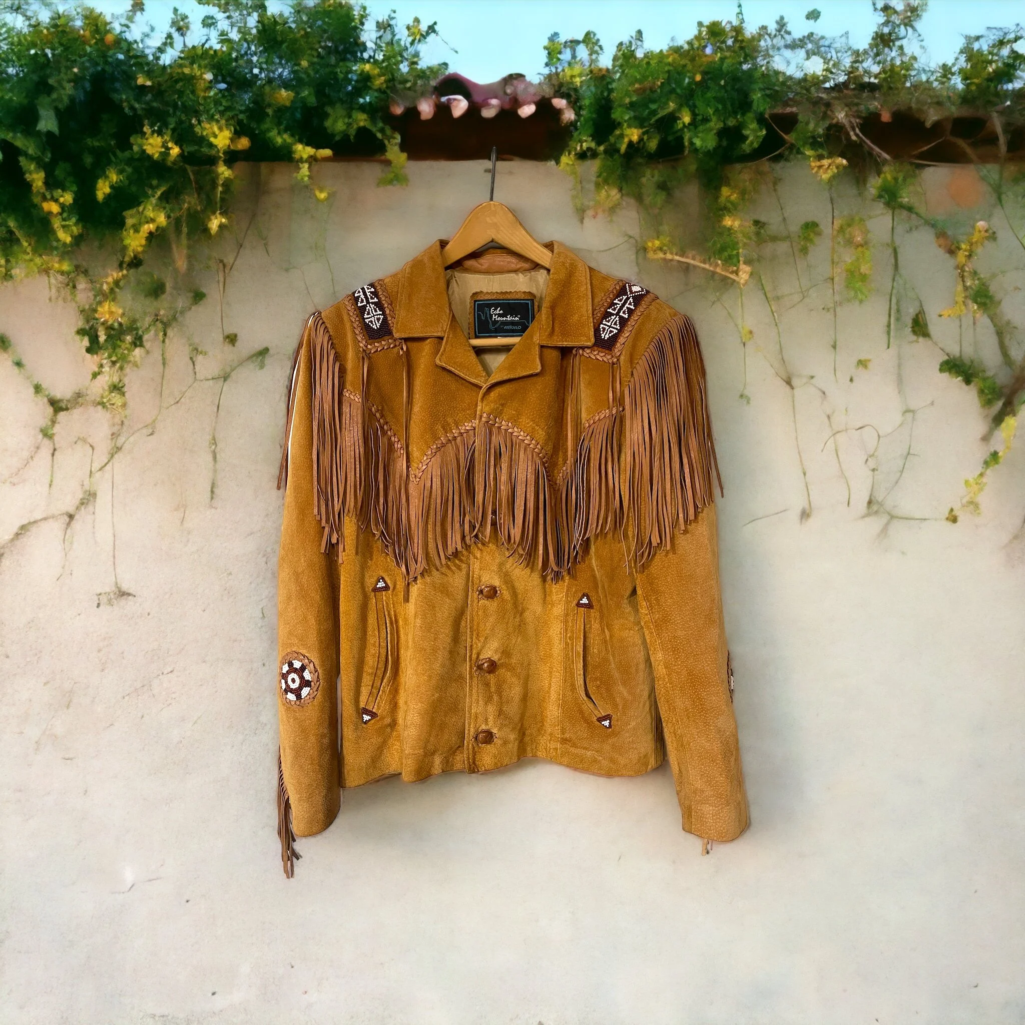Vintage Echo Mountain Arturo Suede Fringe and Beaded Jacket Size 36, Western Wear Made in Mexico, hanging on a concrete wall.