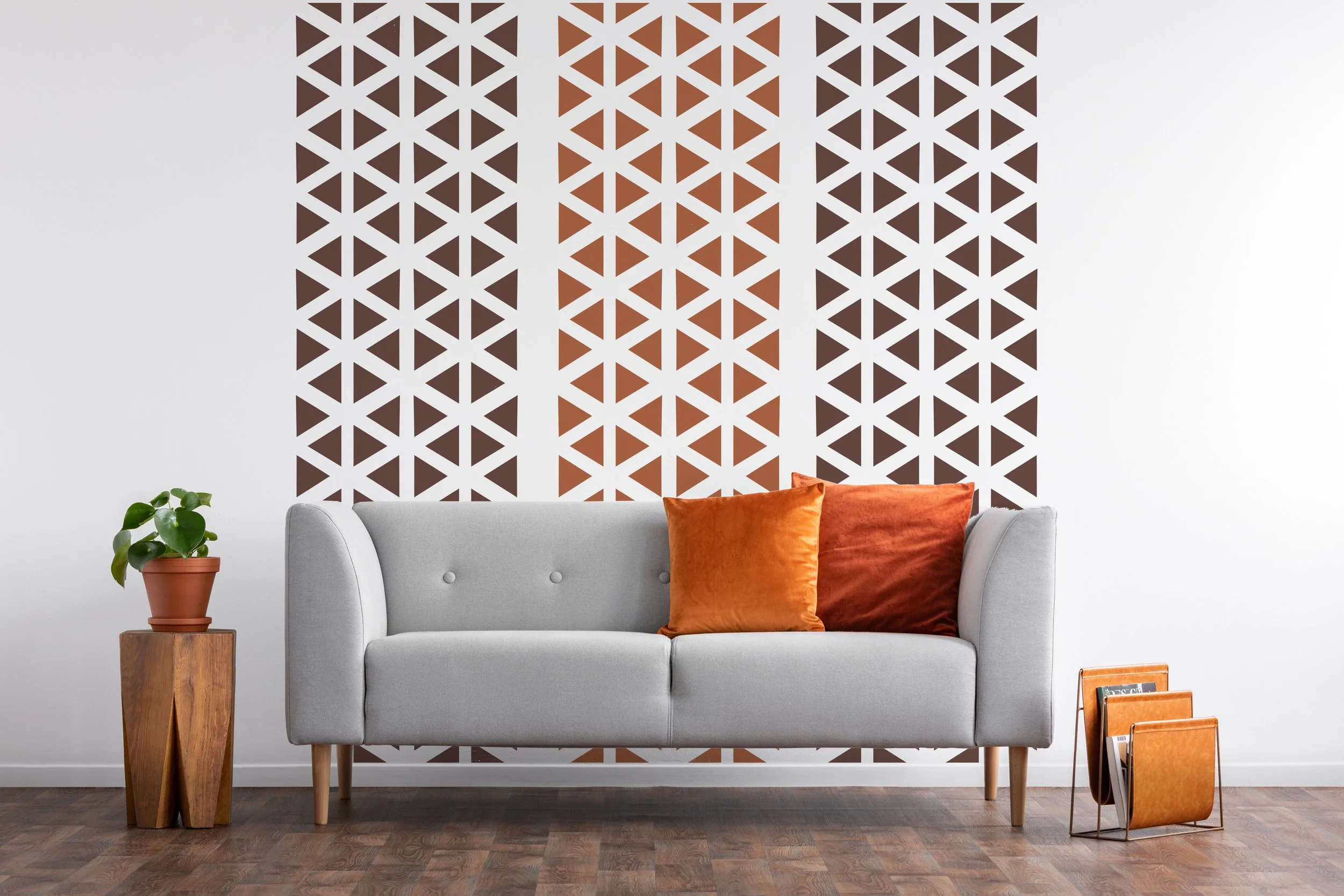 Triangle wall decals by Wall Star Graphics shown in brown and nut brown on a whitewall behind a light grey modern couch with burnt orange throw pillows.