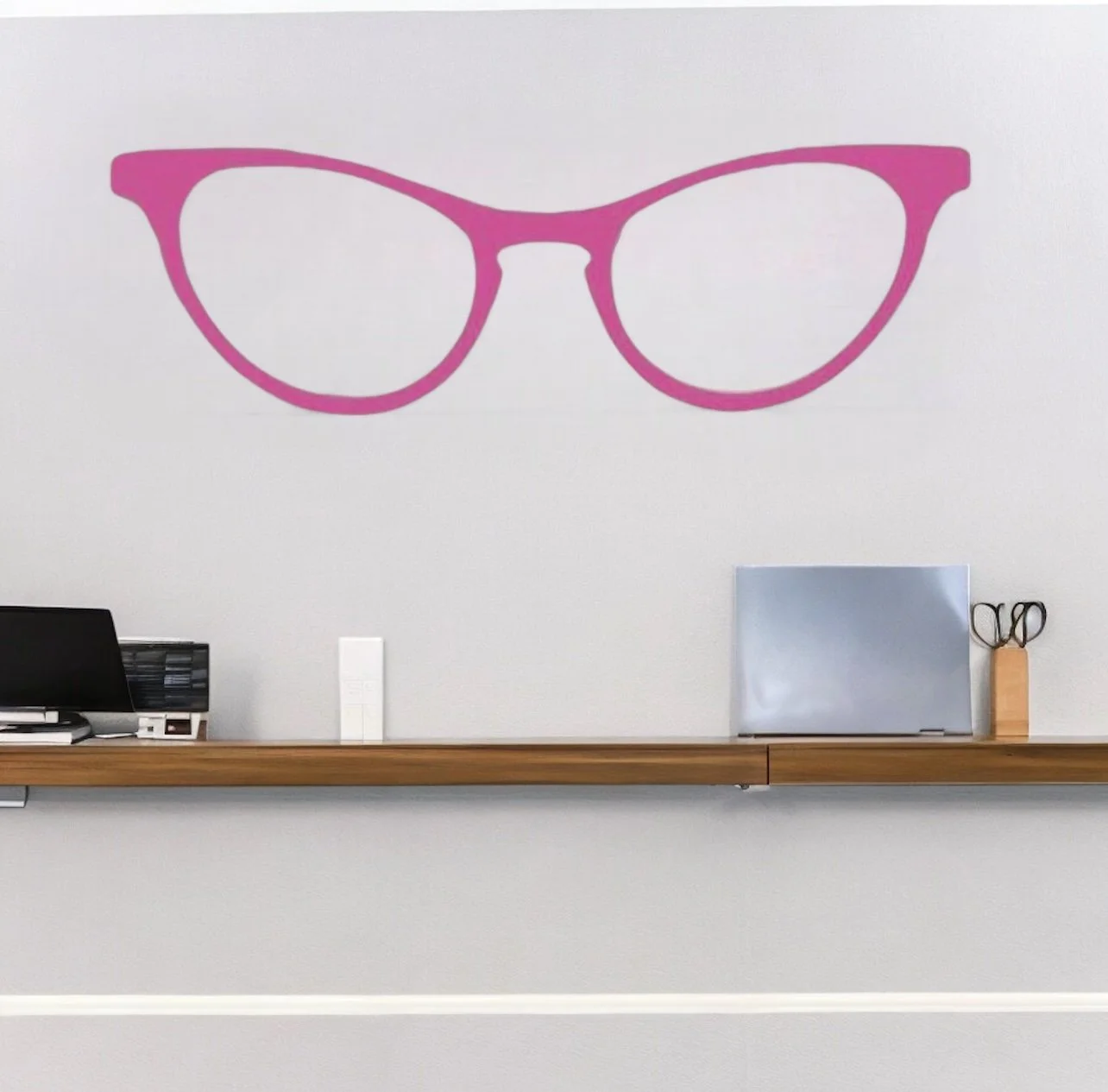 Retro cat eye glasses wall decal shown in pink on a white wall above a desk in an office setting.