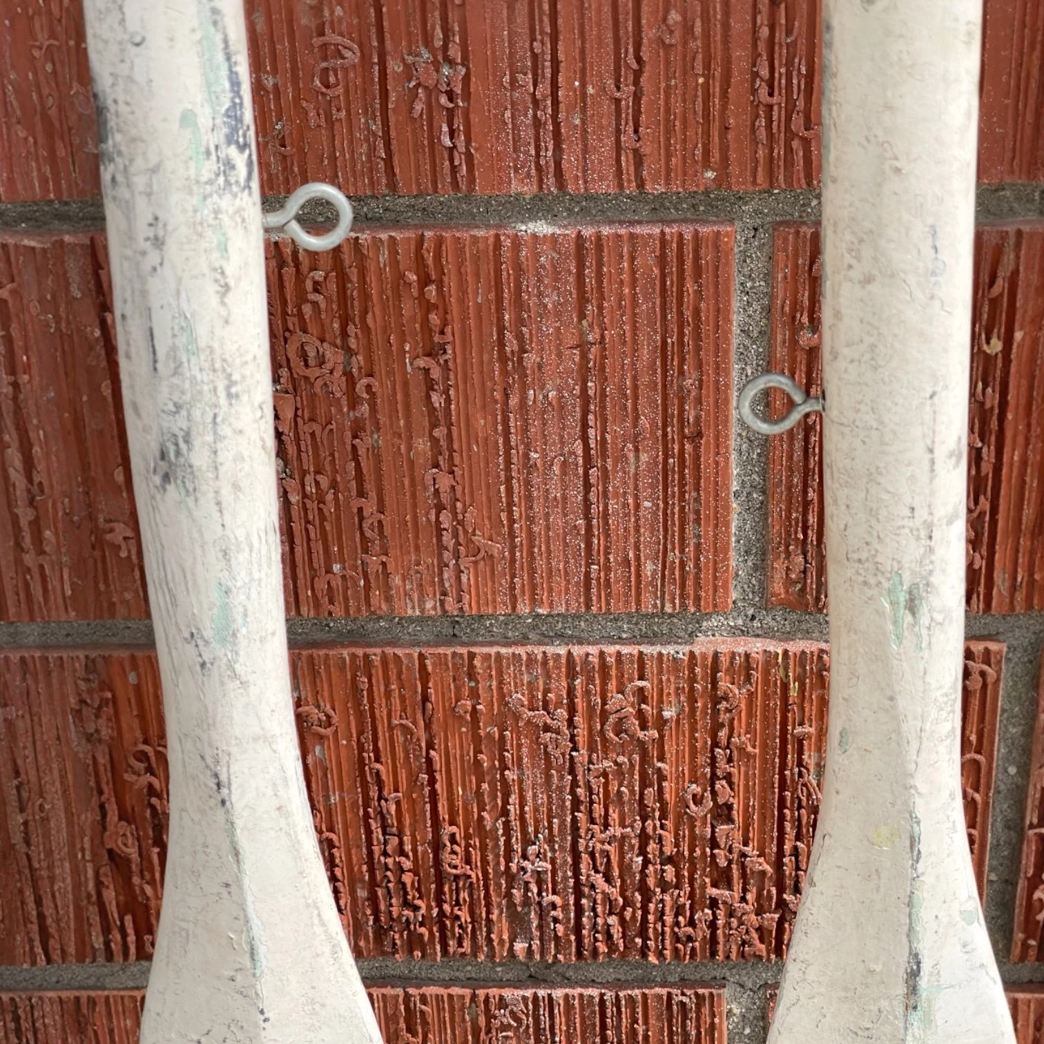Vintage pair of white chippy painted wooden boat oars leaning against a brick wall, complete with oar locks and added eye bolts to use as wall hangings.
