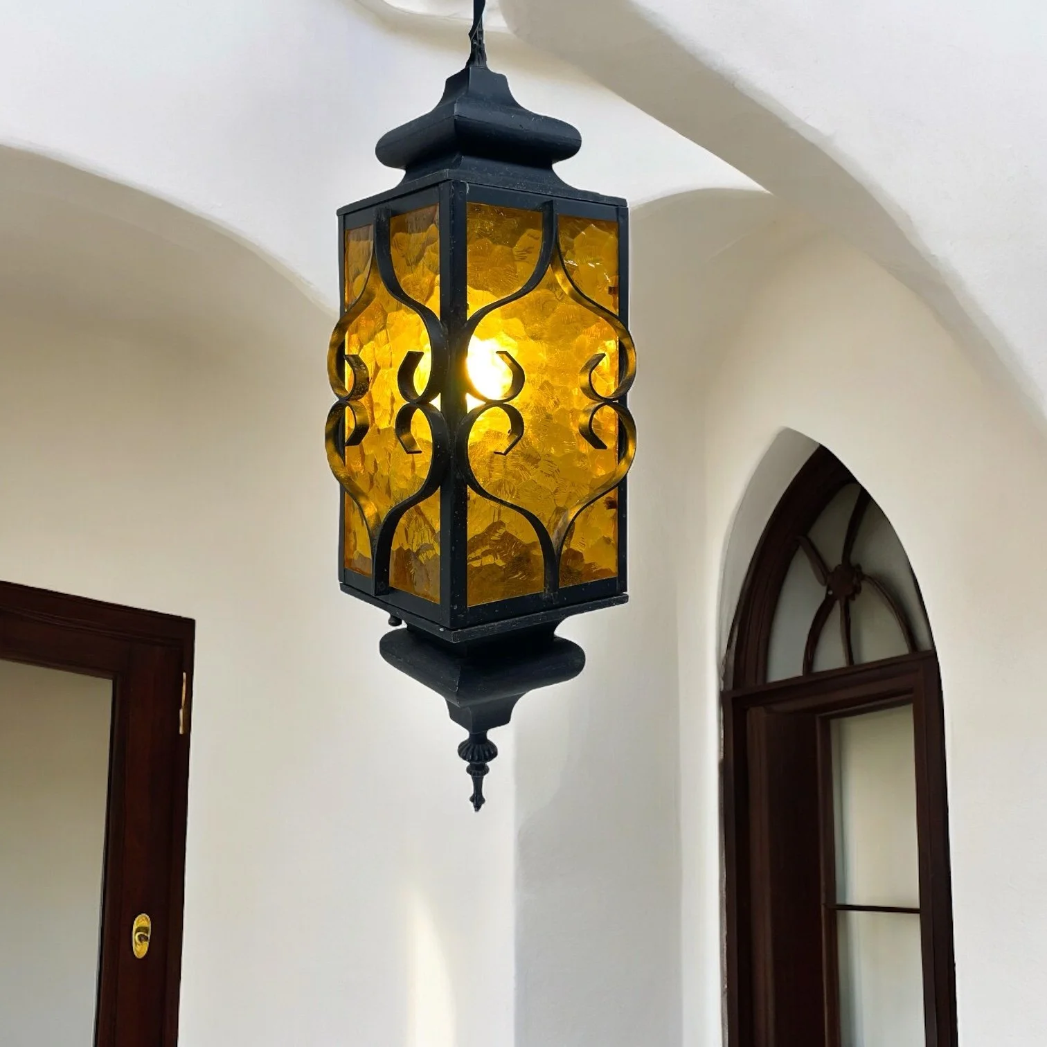 Vintage Spanish Revival hardwired hanging black wrought iron pendant light with amber glass suitable for indoor or outdoor use.