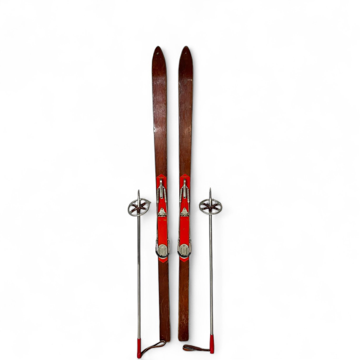 Vintage brown and red wooden Paris Mfg. Co. snow skis with metal bindings and a pair vintage aluminum ski poles with red handle and leather wrist strap.