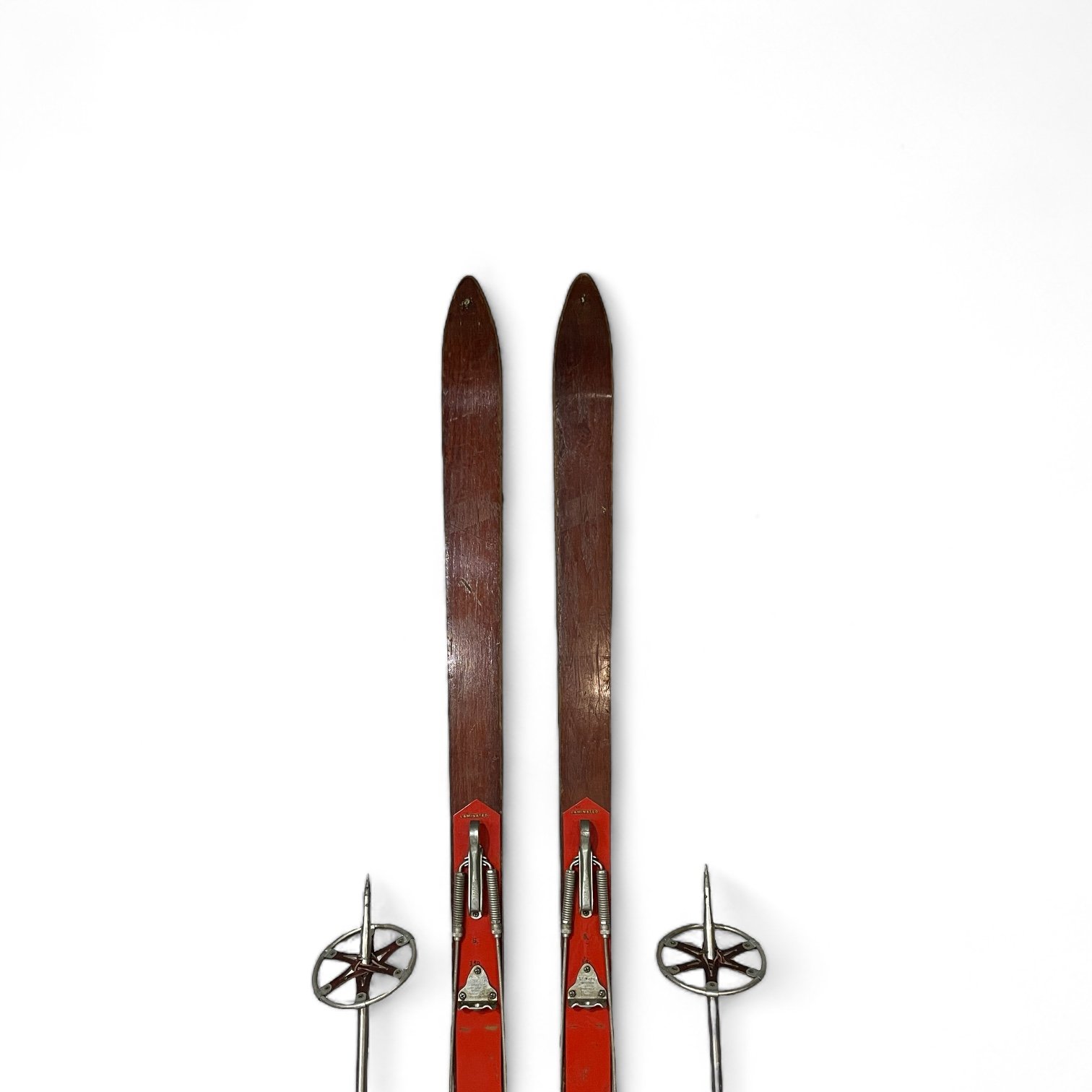 Vintage brown and red wooden Paris Mfg. Co. snow skis with metal bindings and a pair vintage aluminum ski poles with red handle and leather wrist strap.
